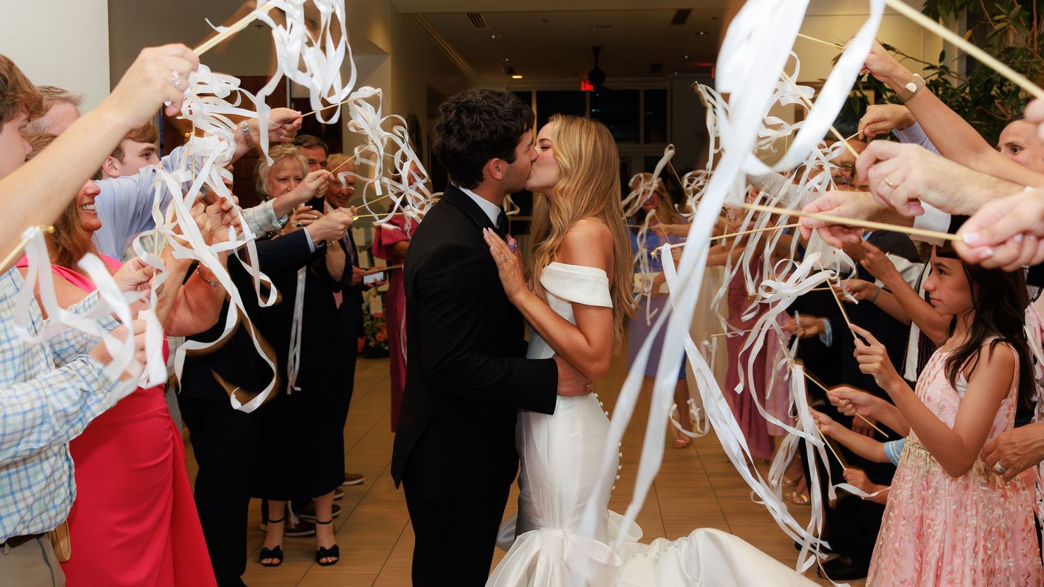 People celebrate at a wedding reception tossing streamer decorations in the air while dancing inside a venue.