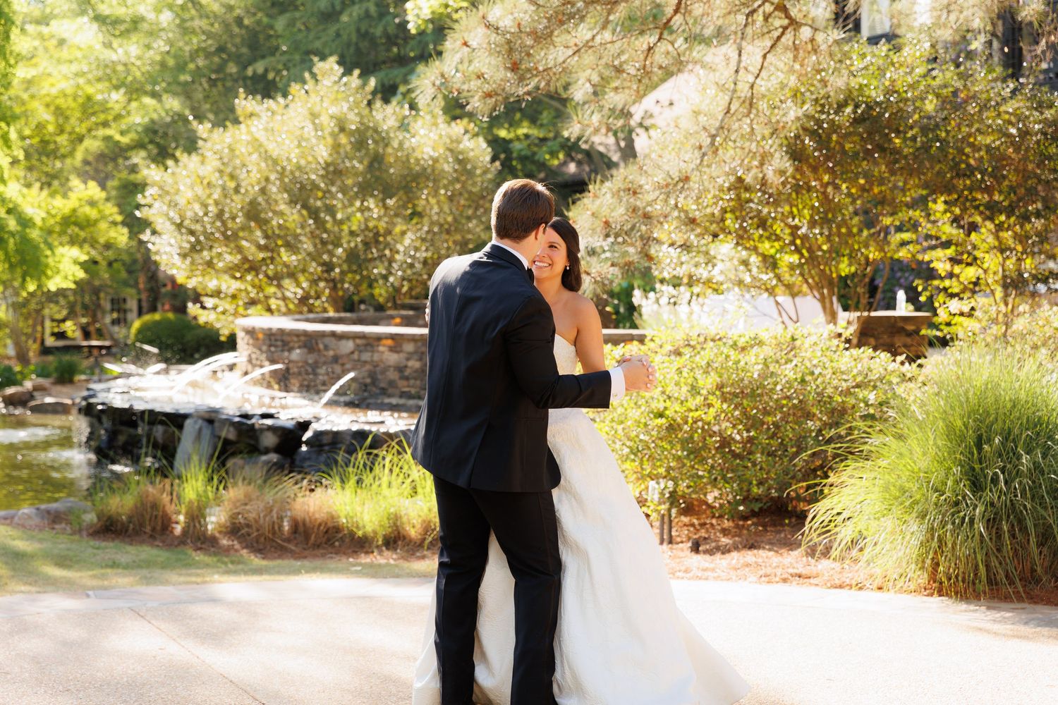 Bride and groom share a romantic moment near a garden pond, surrounded by lush greenery on their wedding day.