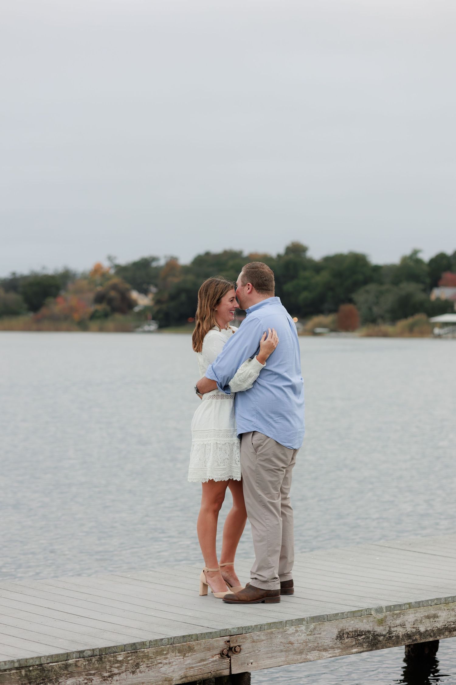 A couple shares a romantic moment on a wooden dock overlooking a serene lake during autumn.