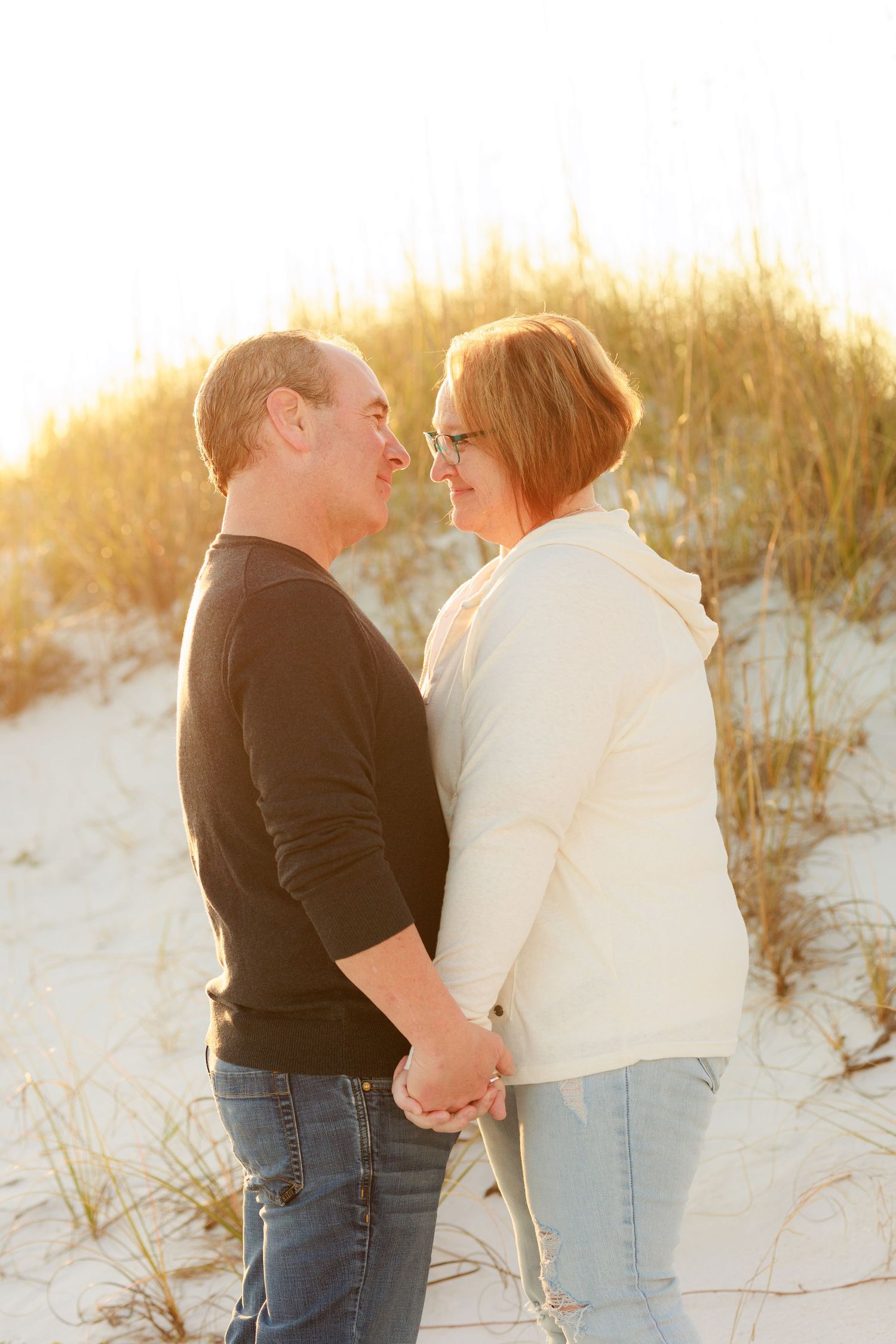 Romantic couple embraces on sandy beach dunes during golden hour sunset.