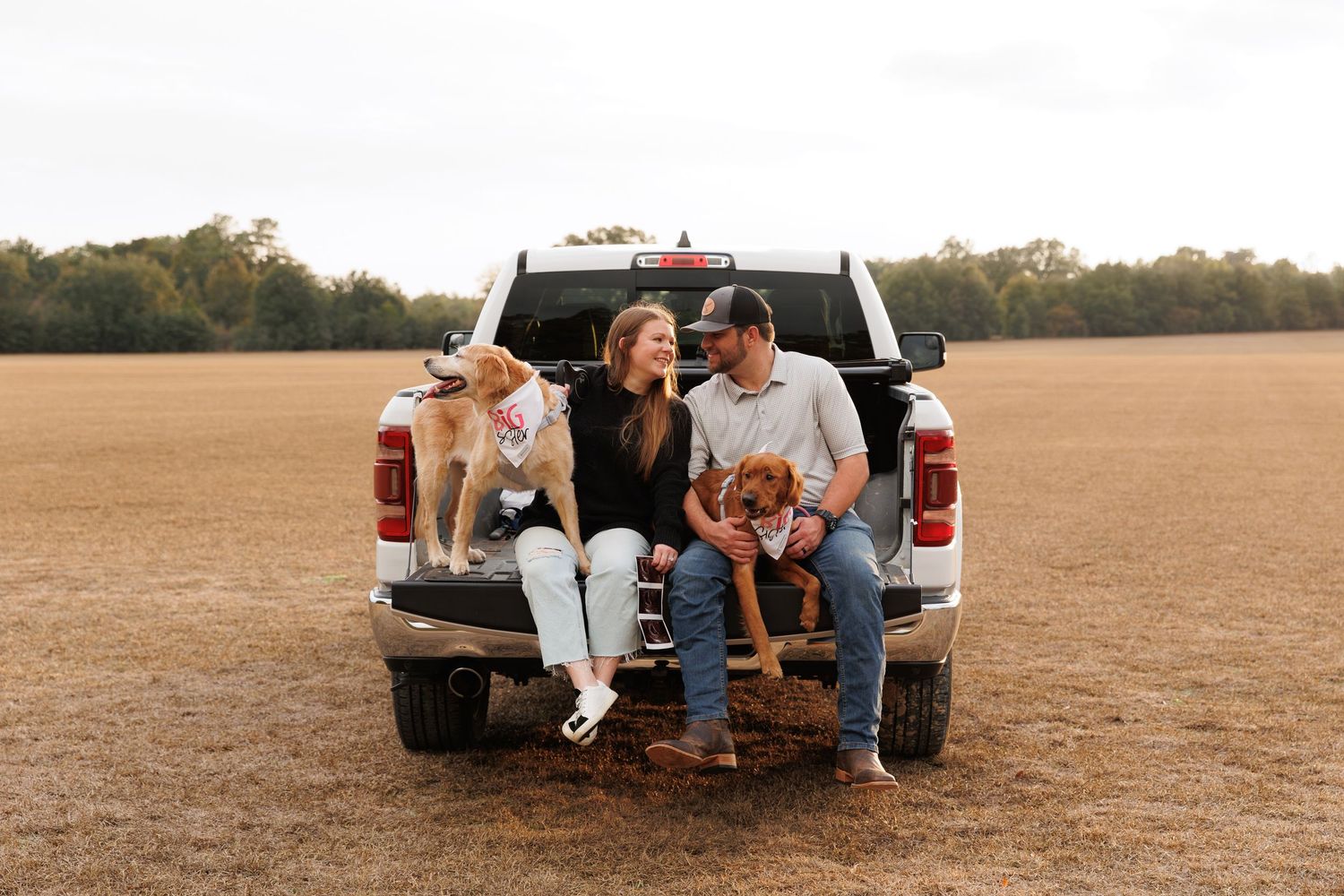Group sitting on tailgate of white pickup truck in open field during golden hour.
