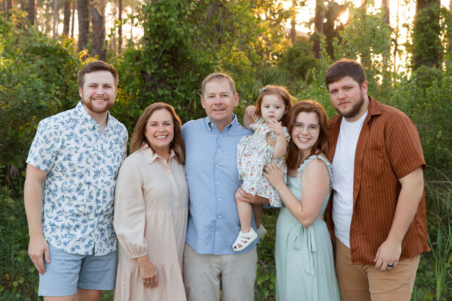 Extended family group poses together outdoors wearing coordinated neutral and mint colored outfits at sunset.