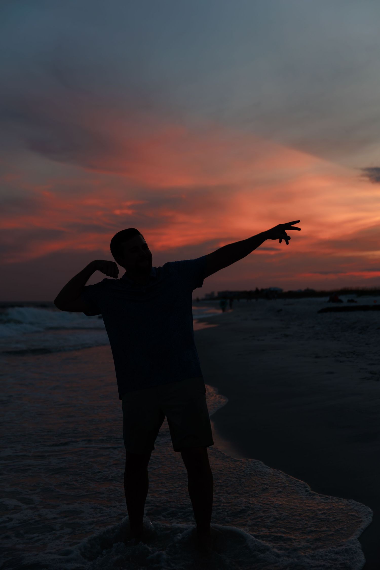 Silhouettes of people gesturing against a dramatic orange and purple sunset over the ocean.