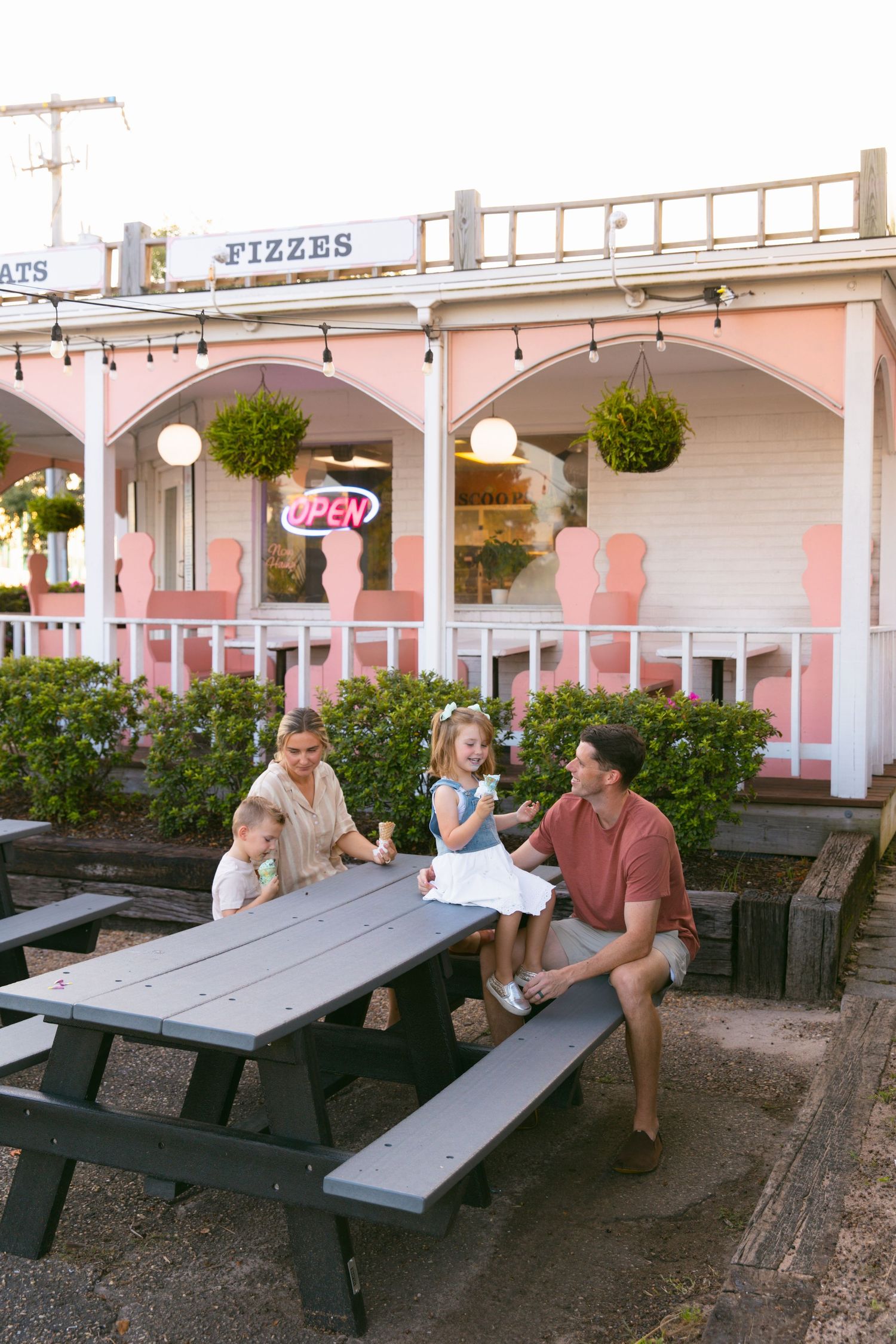 People relax at outdoor picnic tables by a pink retro-styled ice cream parlor.