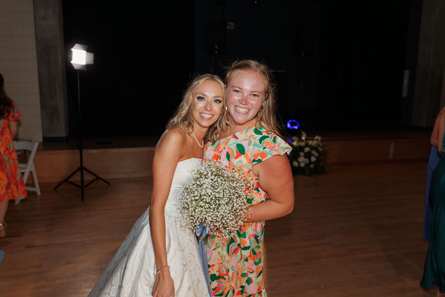 A bride poses with a guest holding a baby's breath bouquet on the dance floor.