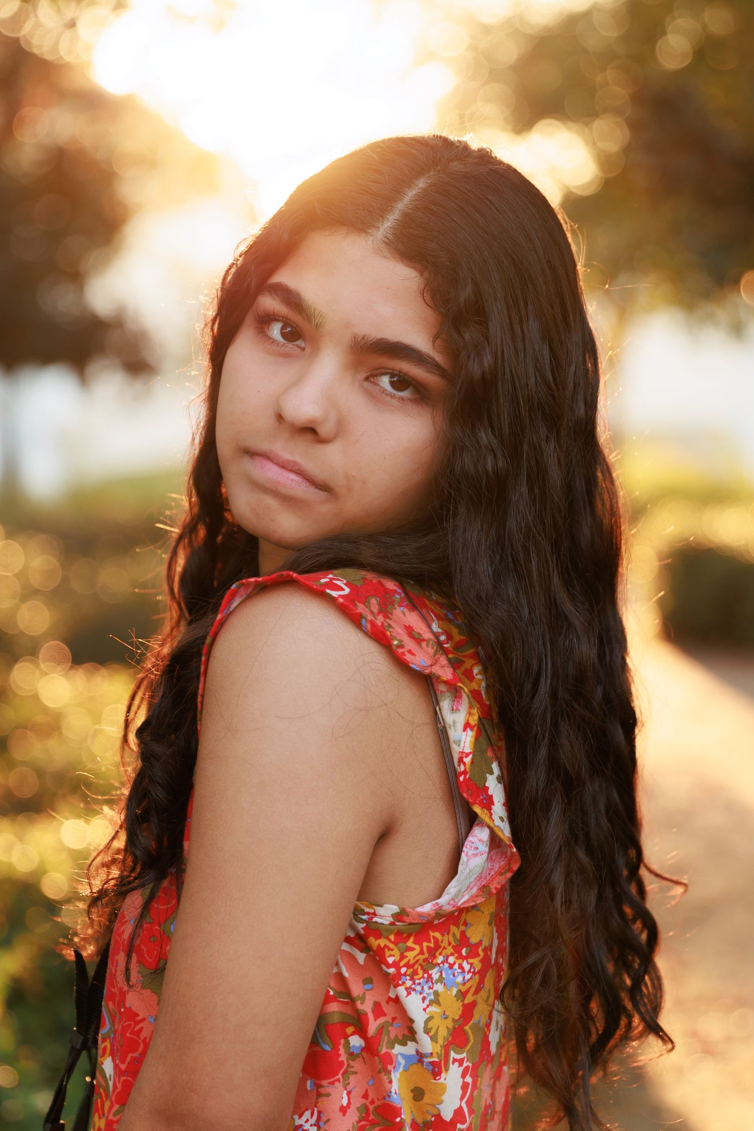 Sunlit portrait in red floral dress with long dark hair.