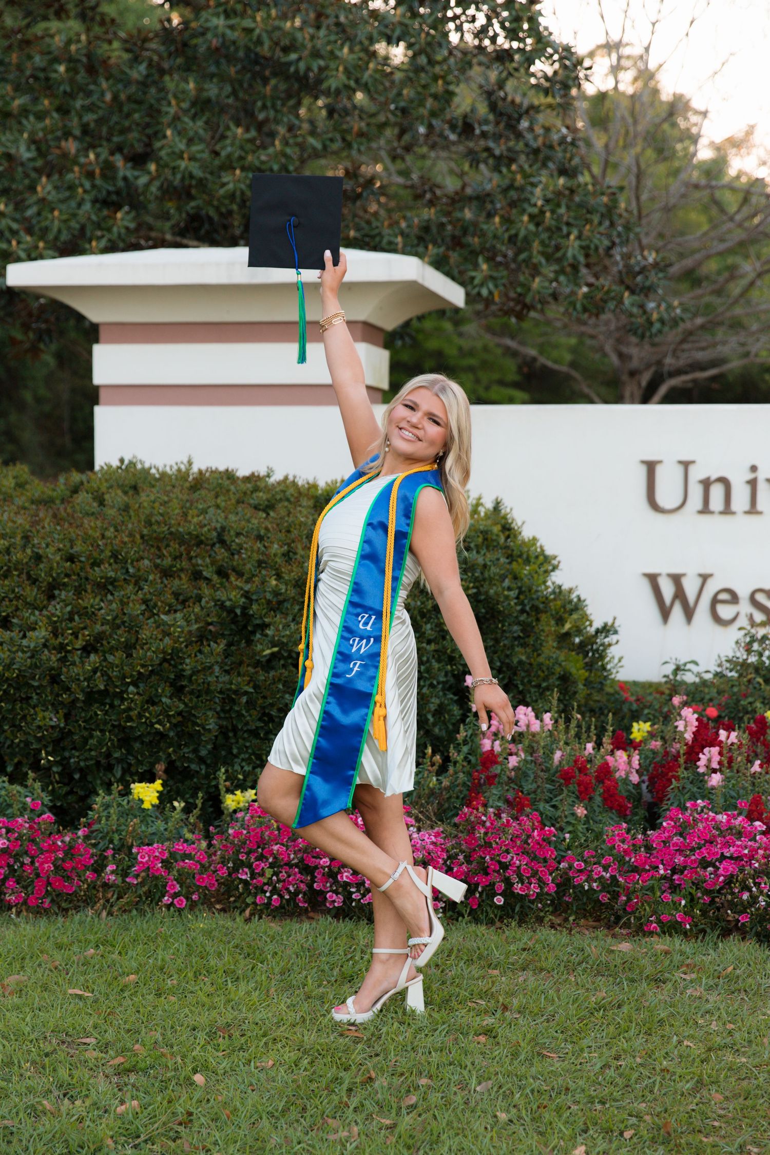 Cheerleader performs a dynamic dance sequence in front of blooming pink flowers and hedges on a grassy lawn.