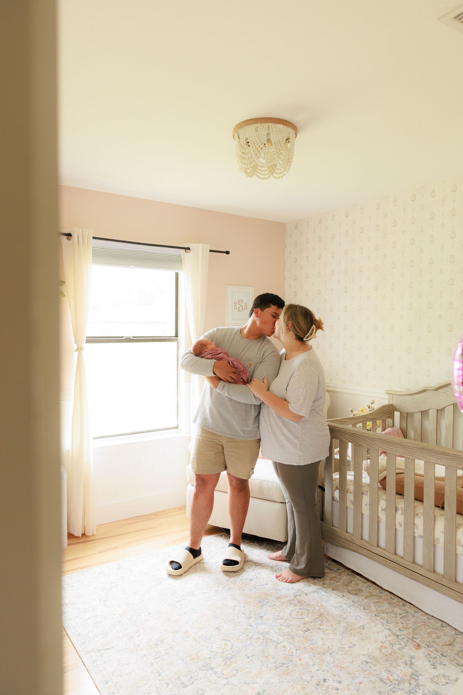 Two people lean over to look at something in an empty nursery room with white walls and carpeted flooring.