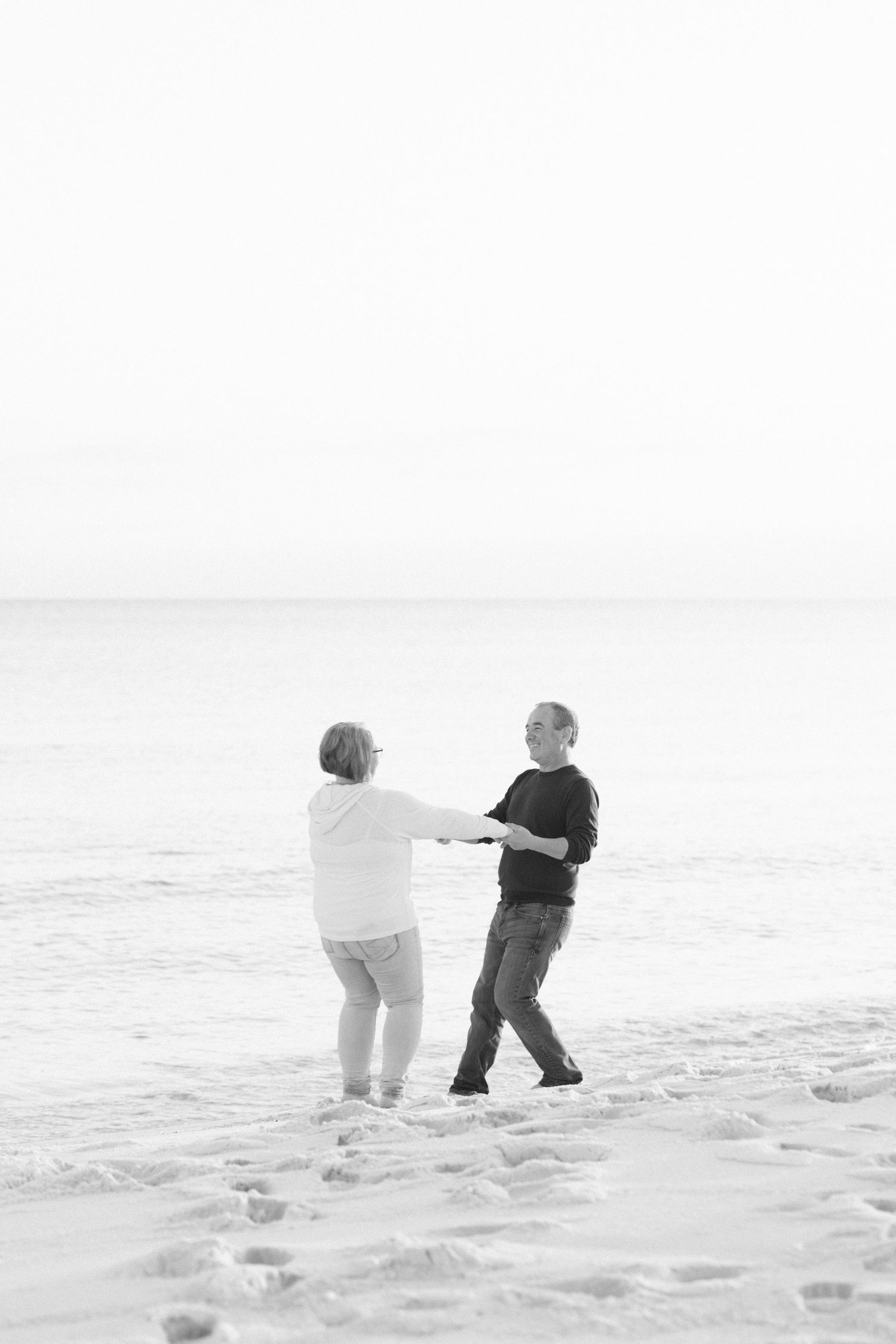 Two people in winter coats walk through deep snow on a bright winter day, creating a minimalist monochrome scene.