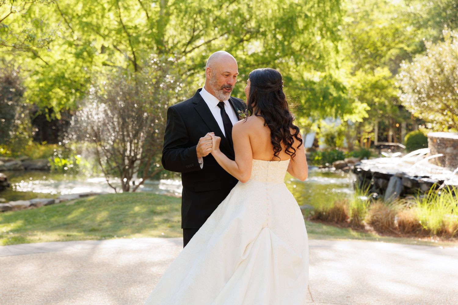 Bride and groom share first dance outdoors surrounded by lush green trees on their wedding day.