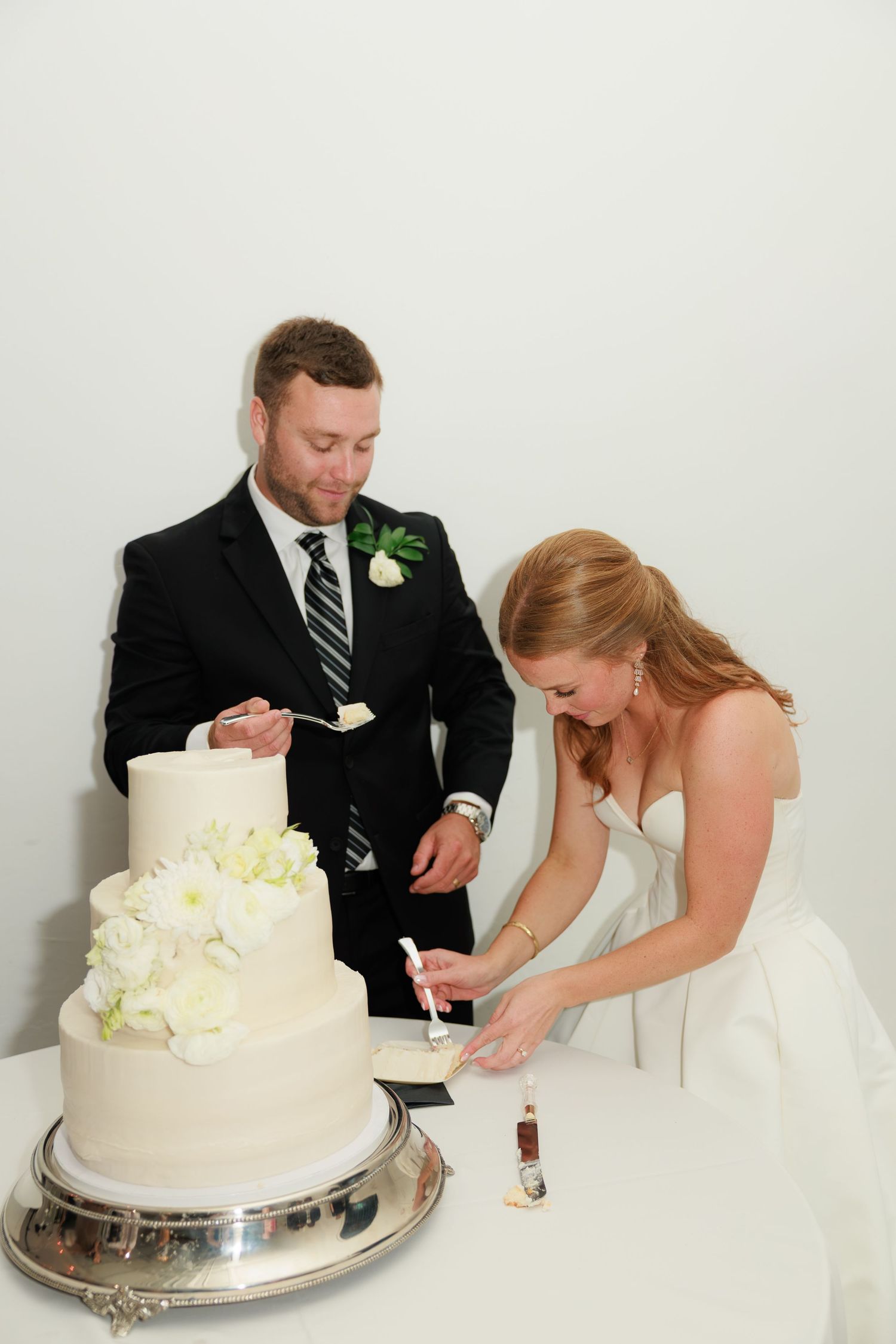 Bride and groom cutting their elegant three-tier white wedding cake adorned with fresh flowers at their reception.