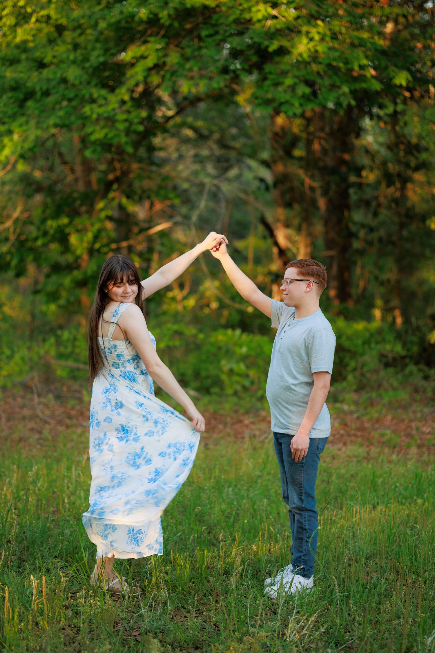 Happy couple dancing together in a sunny green meadow, woman in floral dress being twirled by partner.