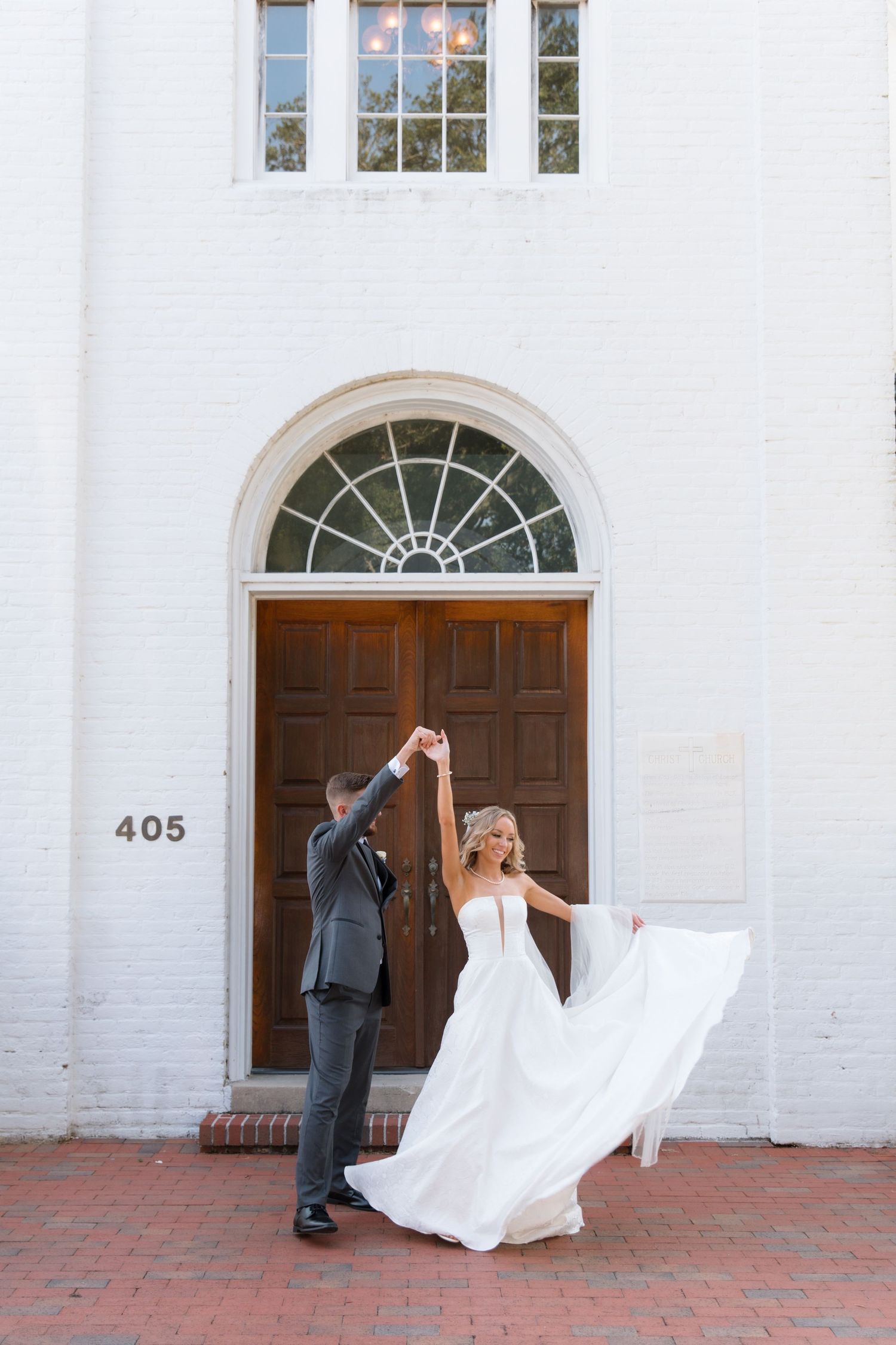 Bride and groom dance playfully in front of white church entrance.