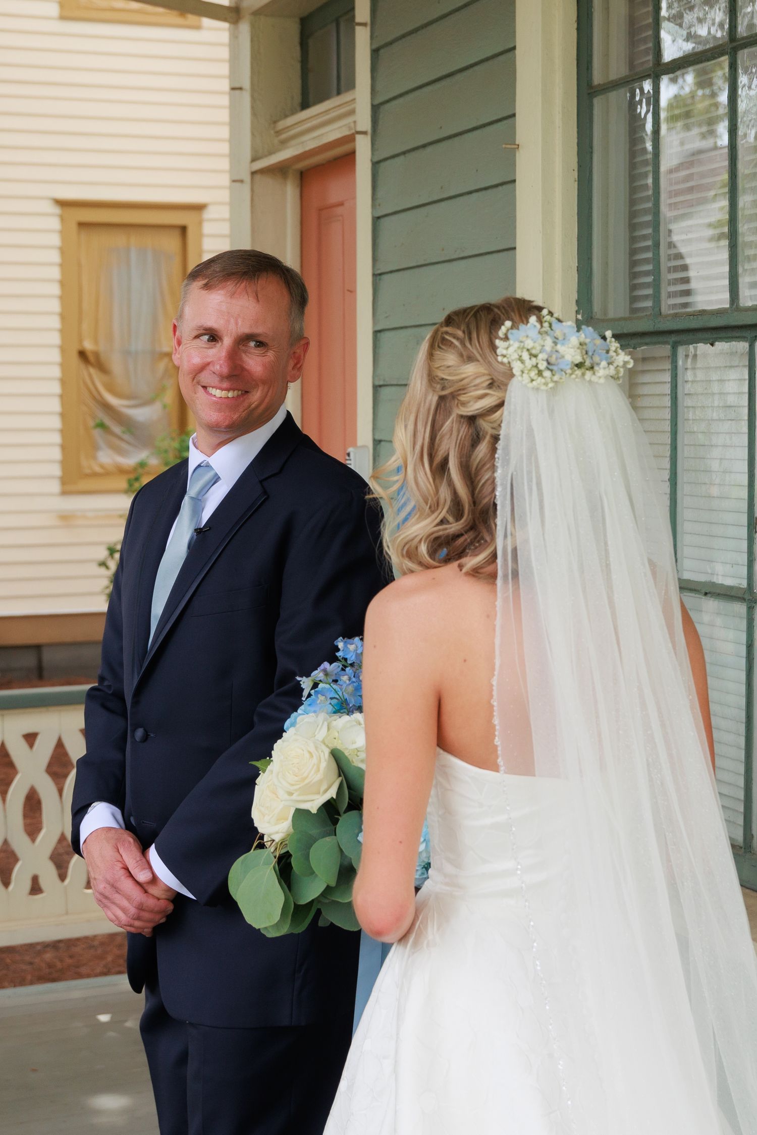 Bride and groom share a first look moment on a vintage porch with green siding.