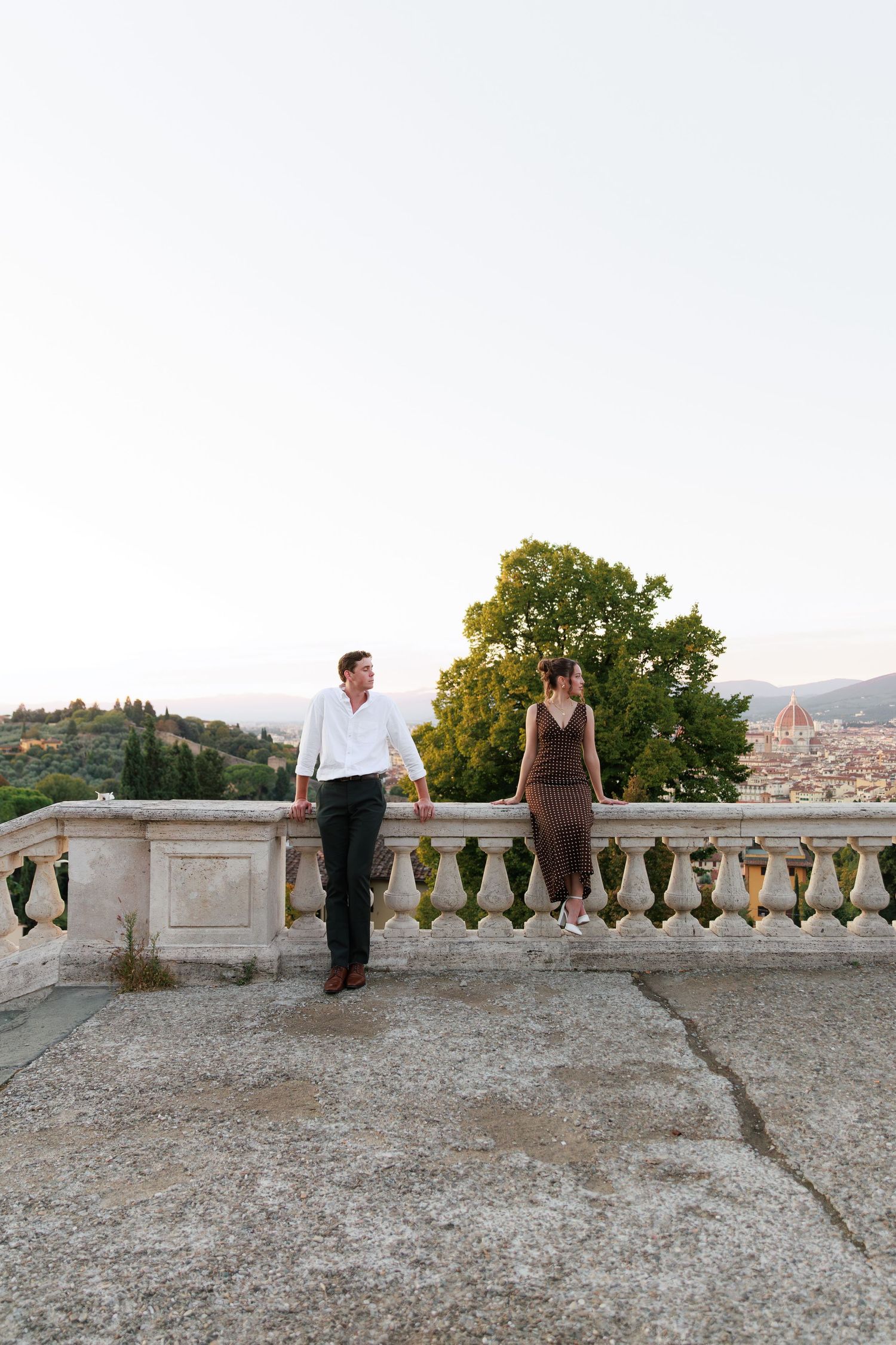 Couple holding hands on scenic Florence overlook terrace with cathedral dome visible at dusk.