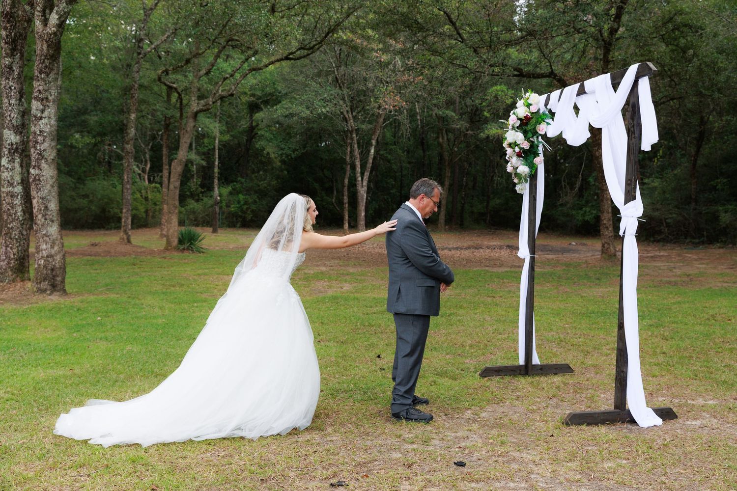 Wedding party stands in line outdoors with white fabric banners flowing between them in a garden setting.