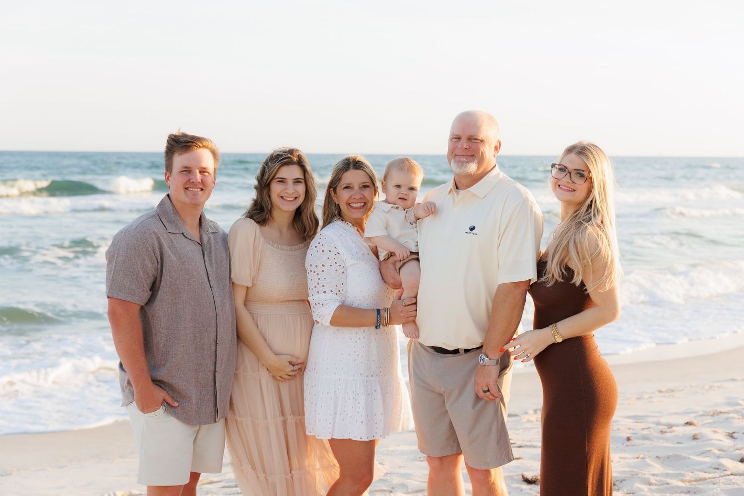 Family of six posing together on a sandy beach at sunset with ocean waves in the background.