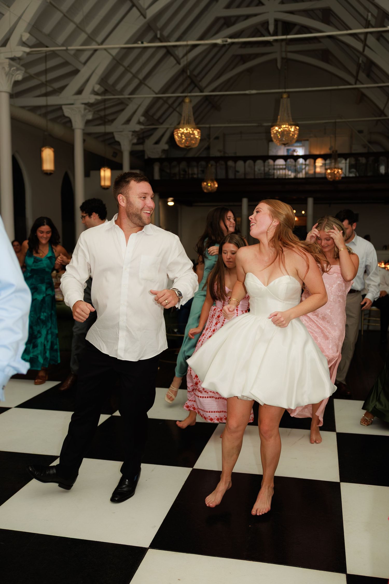Joyful bride and groom dancing barefoot on a black and white checkered dance floor at their wedding reception.