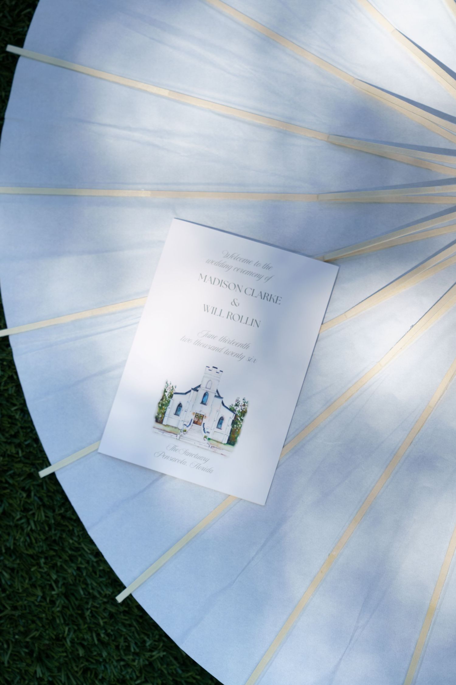 Elegant wedding program on a white parasol umbrella, featuring watercolor church illustration for Madison Claire and Will Rollin.