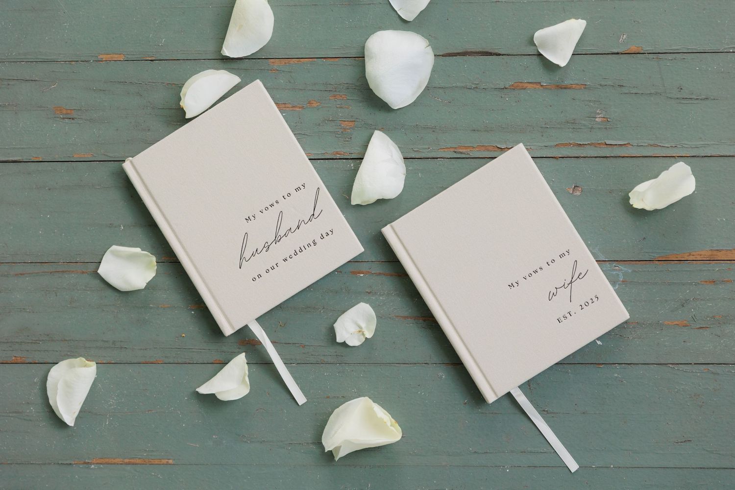 White rose petals scattered on a weathered teal wooden surface with small white cards.