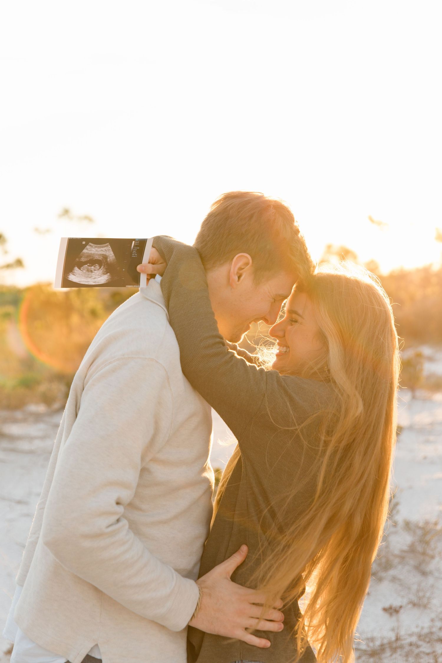A romantic couple embraces during a golden sunset photoshoot on the beach with warm glowing light.