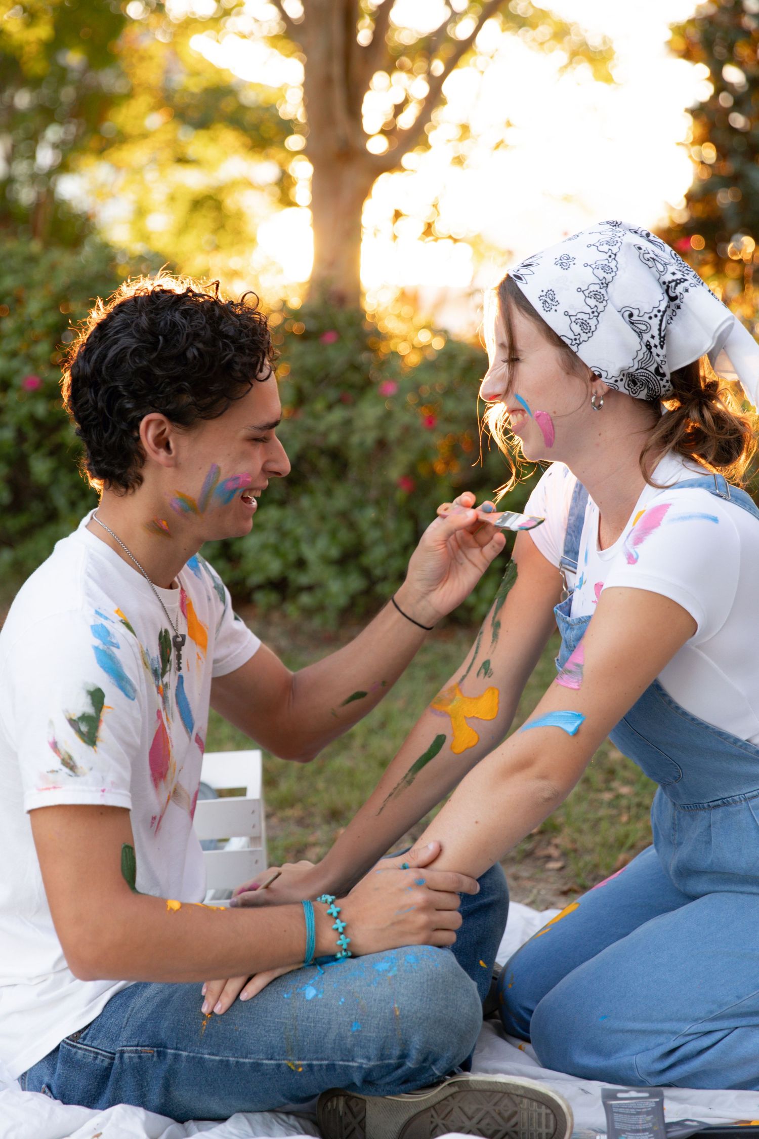 Couple playfully smearing cake frosting on each other's faces during sunset engagement photoshoot outdoors.