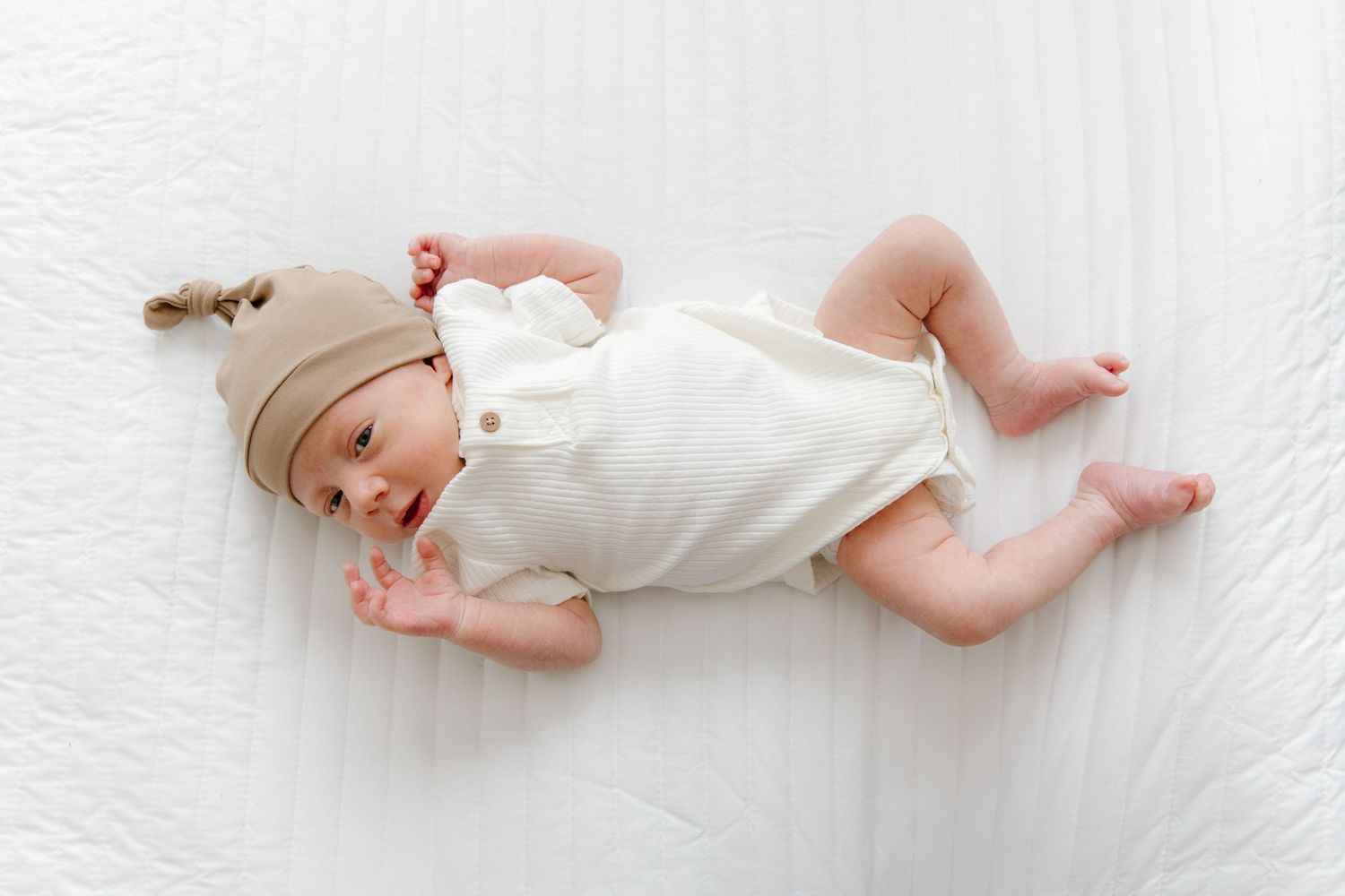 Four connected images showing a sleeping newborn baby in white clothing lying on a white blanket.