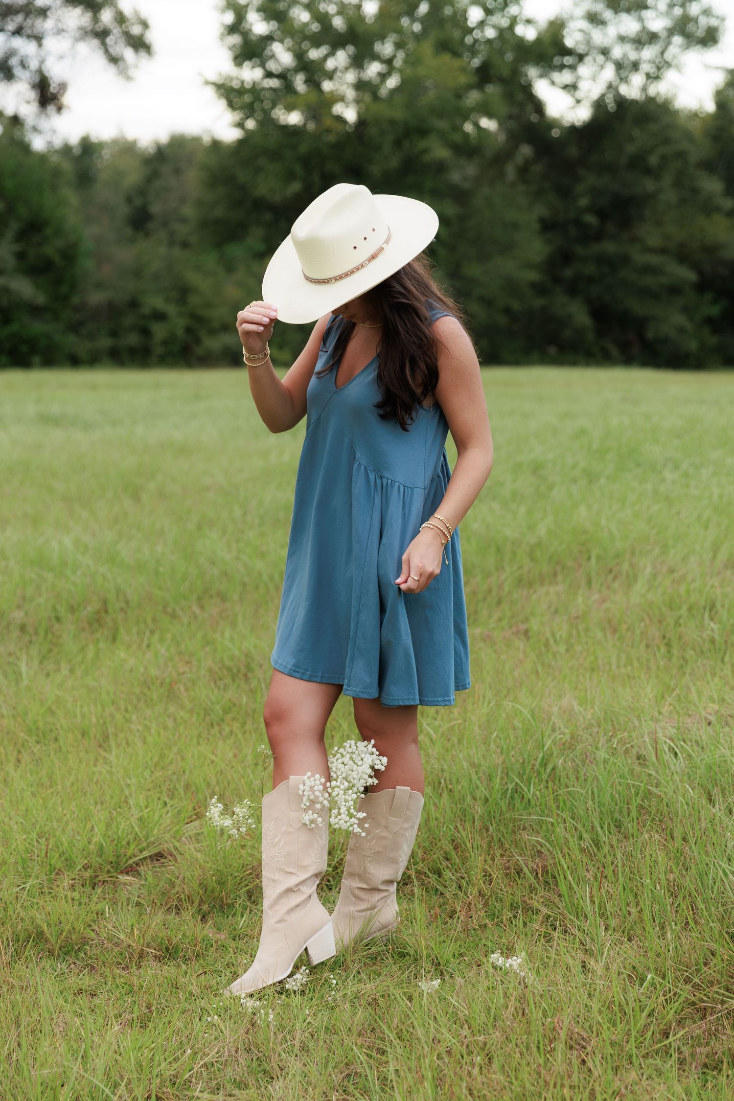 Summer fashion shoot featuring a flowy blue dress and western boots in a pastoral setting.