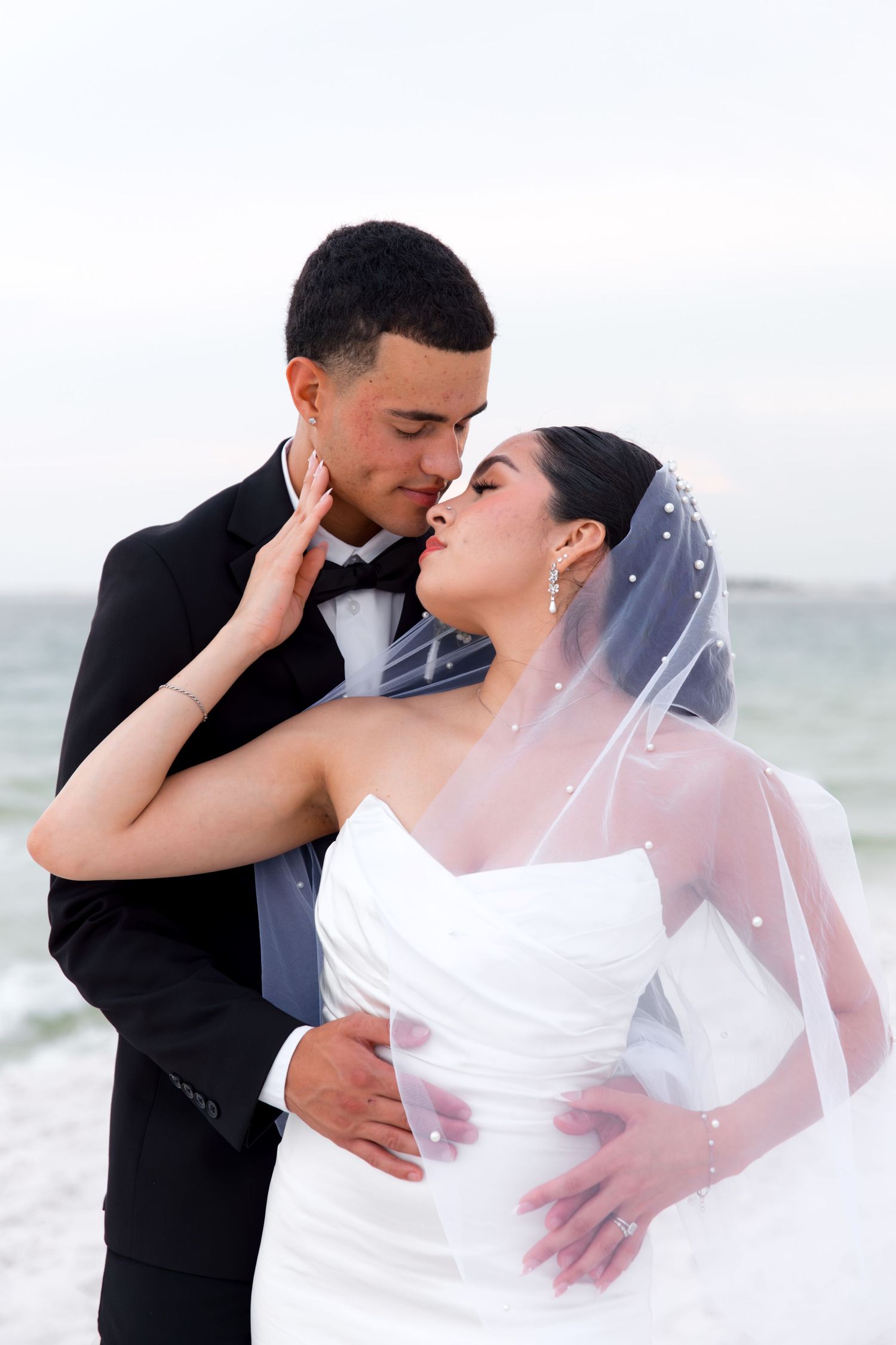 Romantic beach wedding portrait of couple embracing with flowing veil.