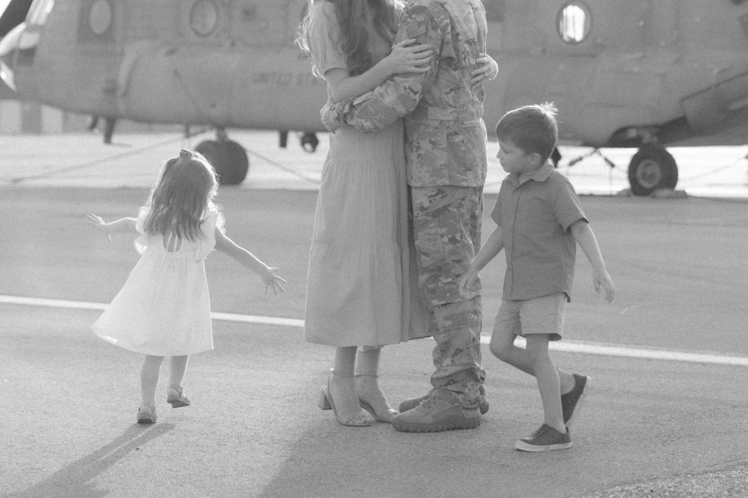 Family gathers near military helicopter during black and white photo session.