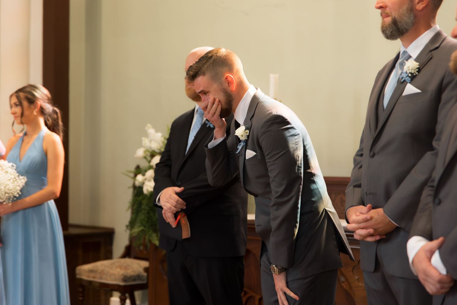 Groomsmen in dark suits stand in formation during church wedding ceremony.