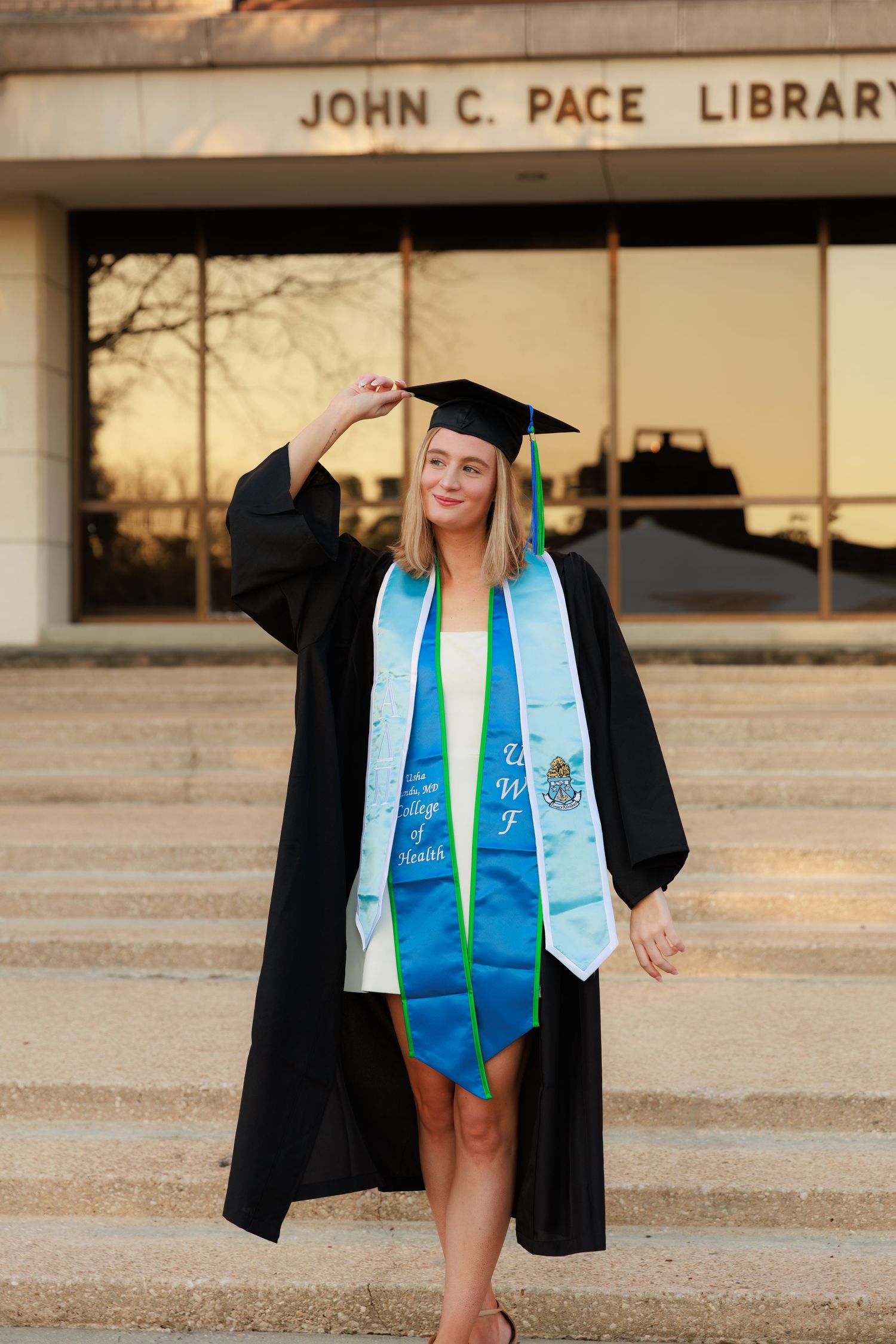 Graduate in cap and gown poses in front of John C. Pace Library during sunset graduation photoshoot.