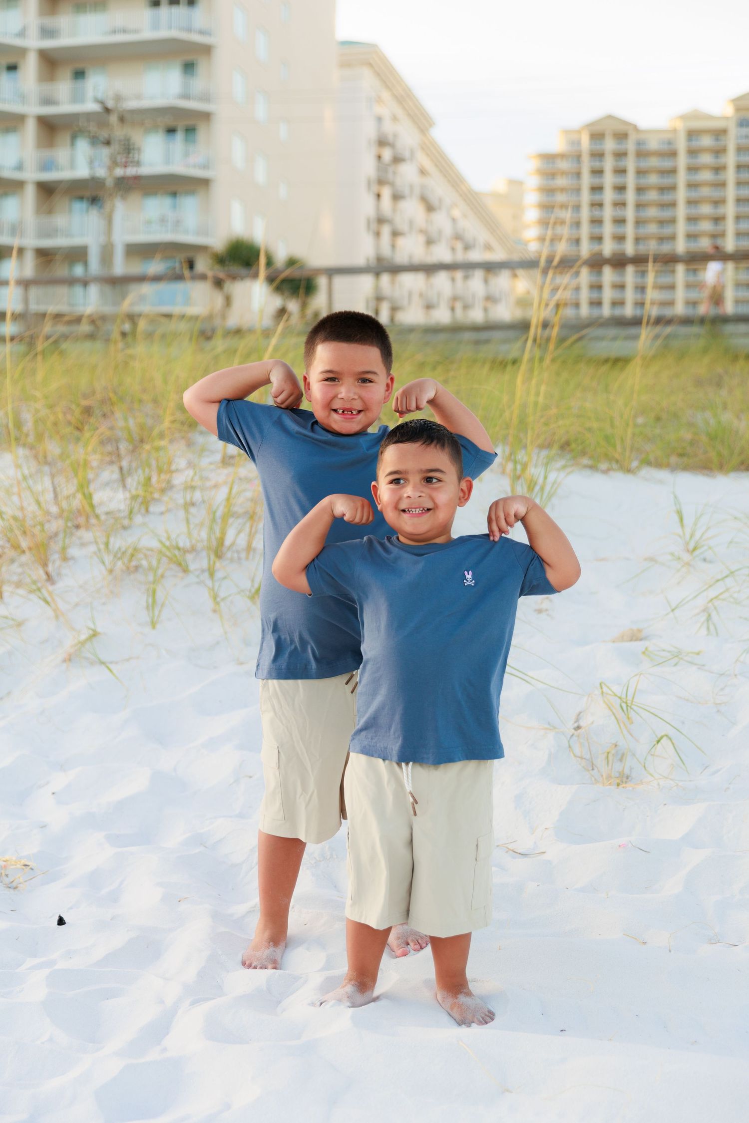 Two children playing and posing together on a white sandy beach with beachfront condos in the background.