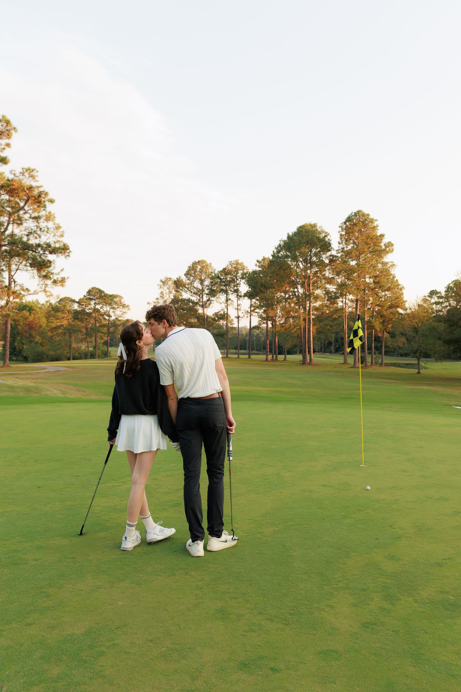 A couple practicing golf together on a lush green course during golden hour.