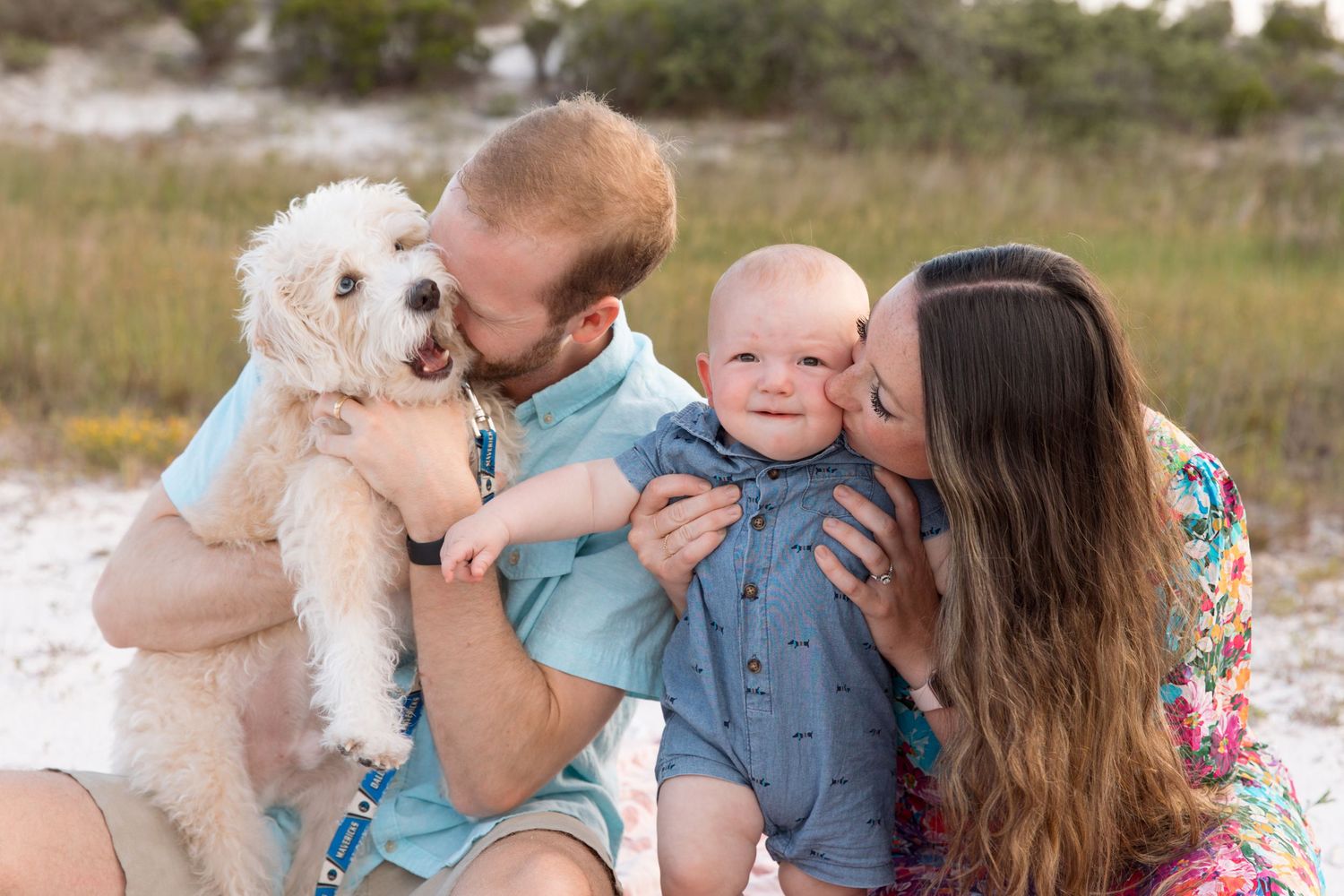 A family shares tender moments with their white dog on a sandy beach during a photo session.