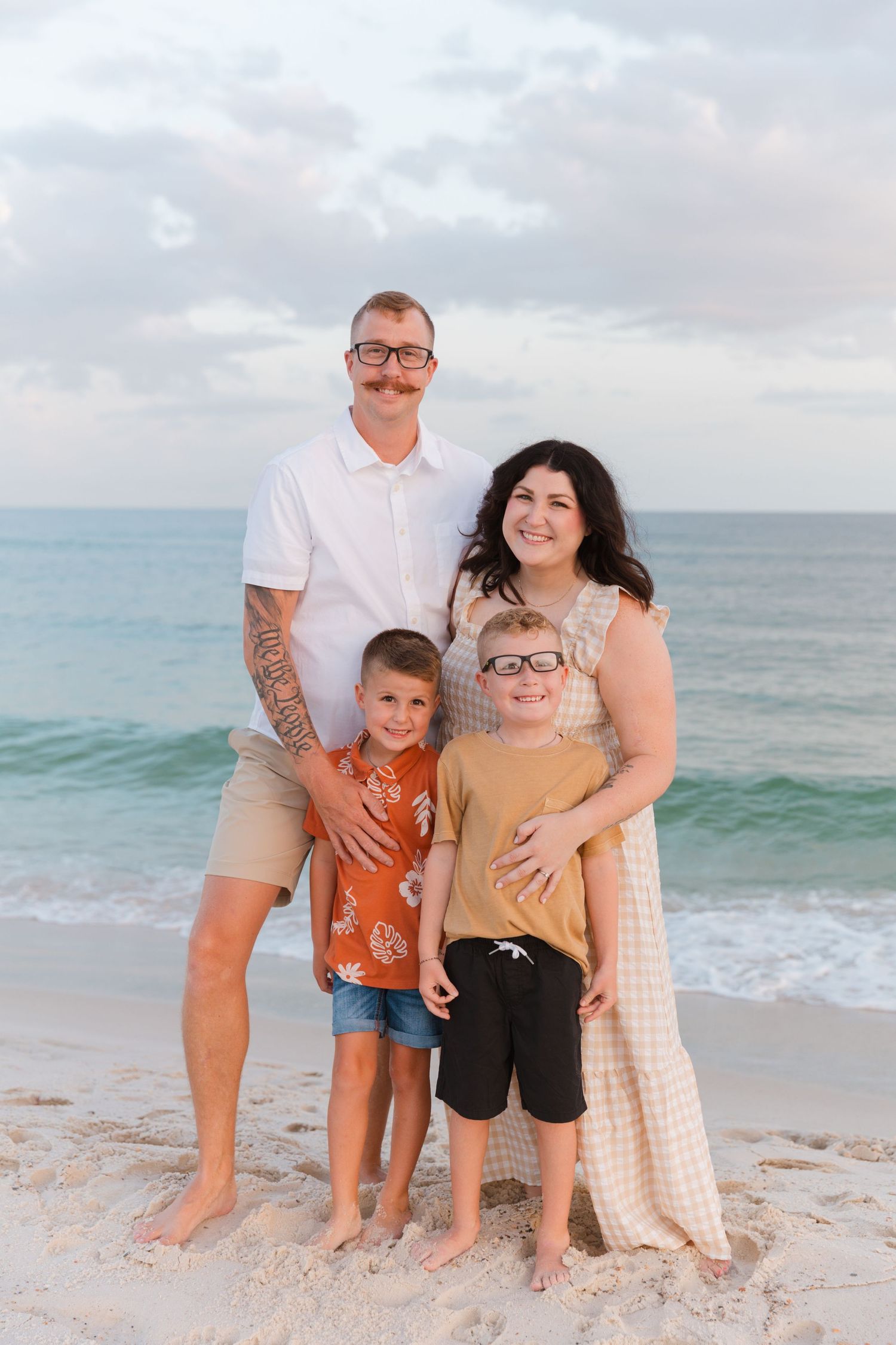 A happy family poses together on a sandy beach at sunset with the ocean waves in the background.