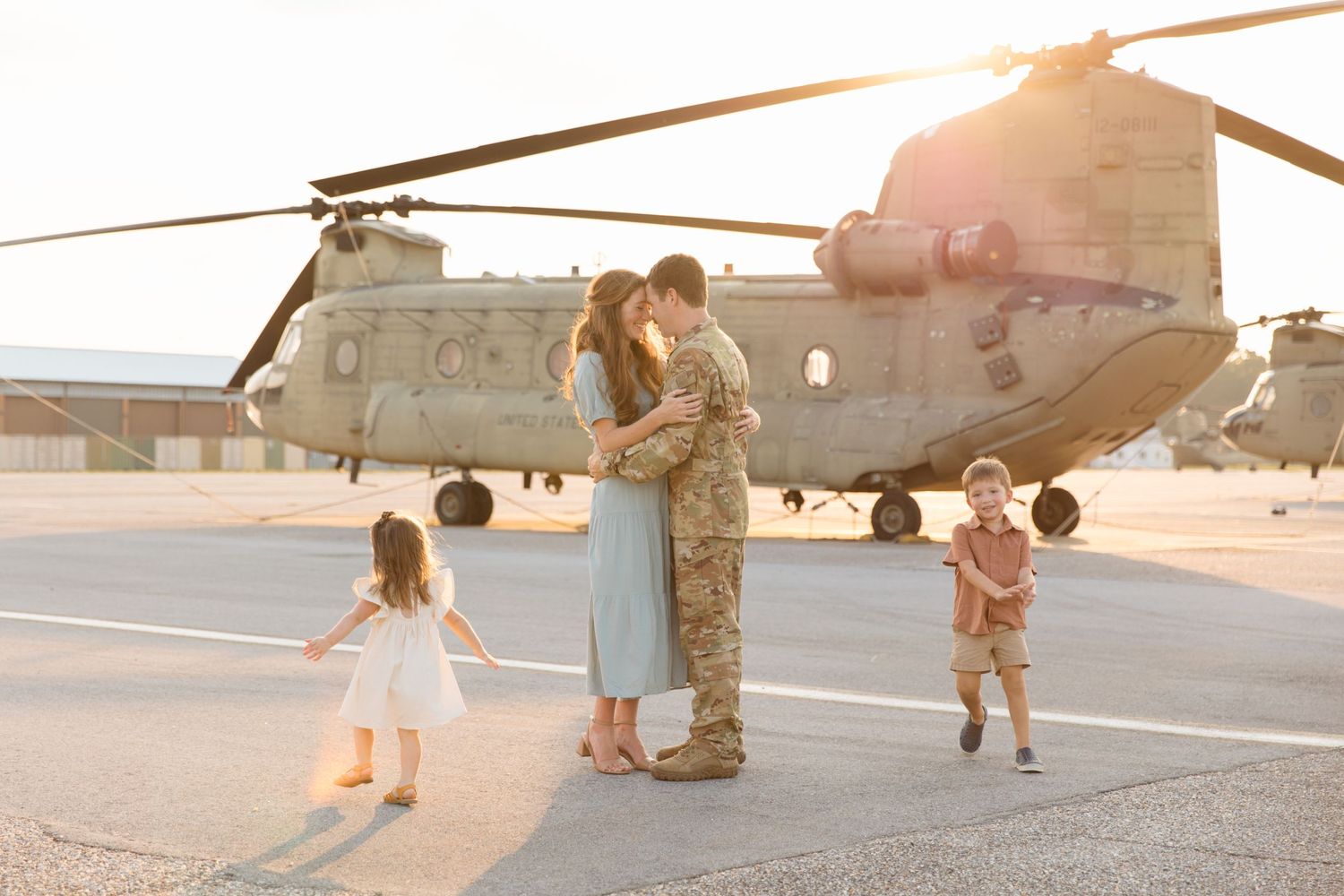 Family reunites with service member in front of military helicopter at sunset.