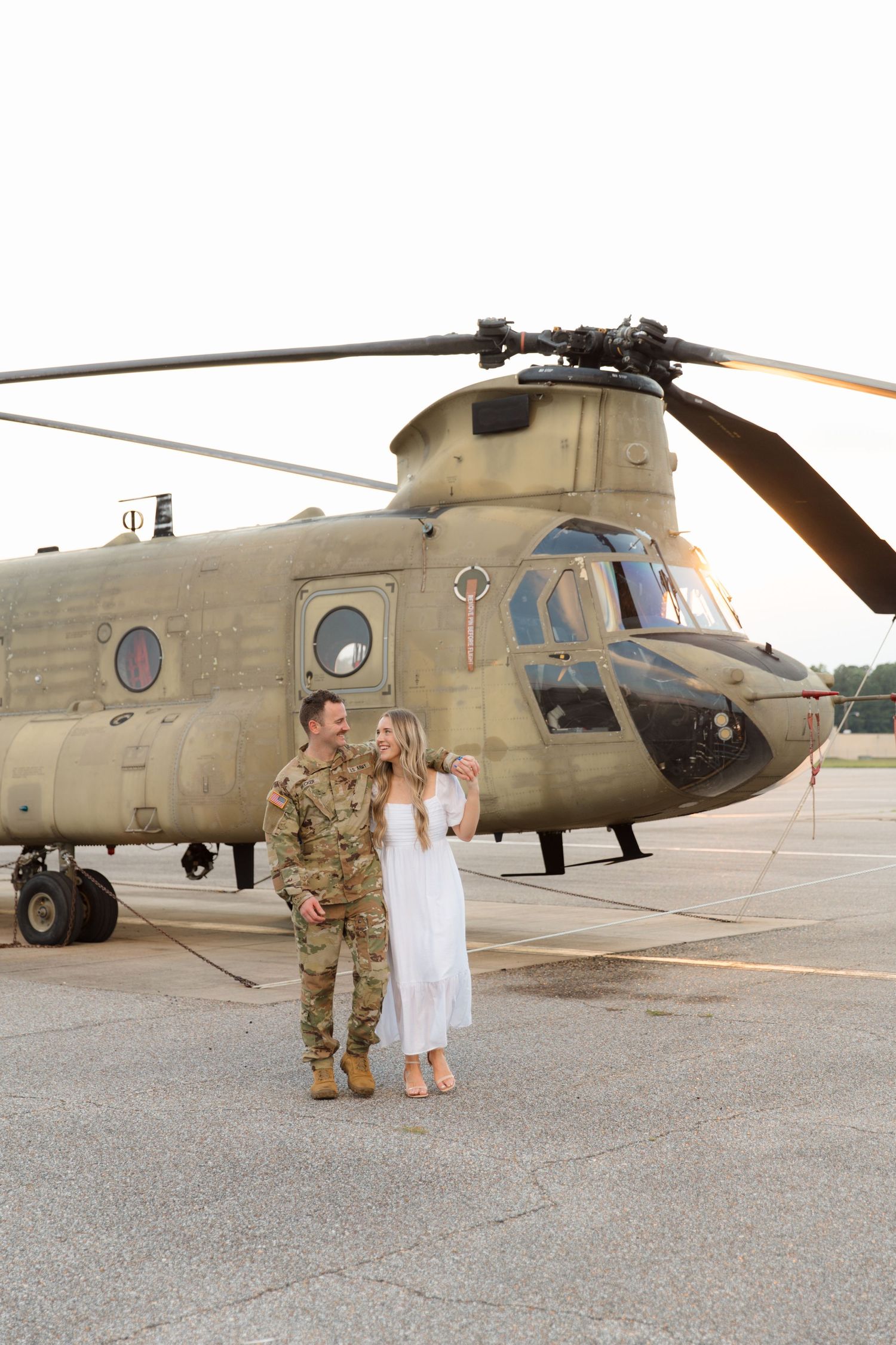 Couple posing for a photo in front of a military Chinook helicopter.