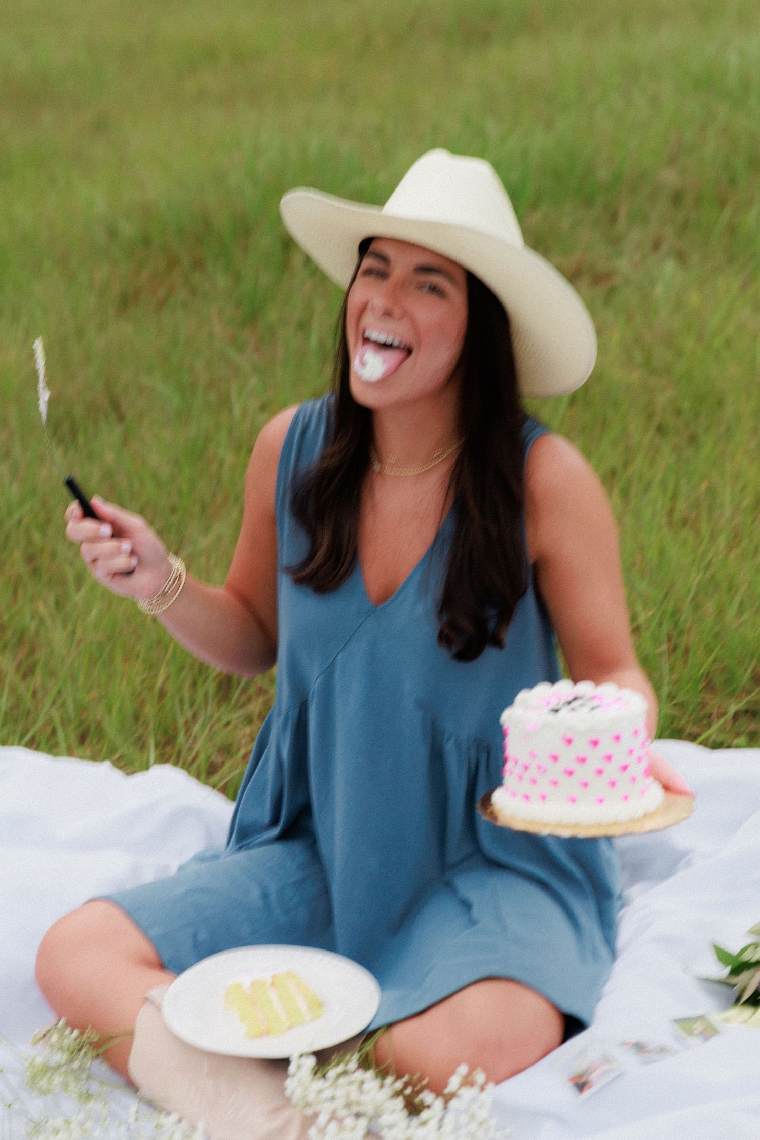 Someone in a blue dress and cowboy hat enjoying cake at an outdoor picnic.