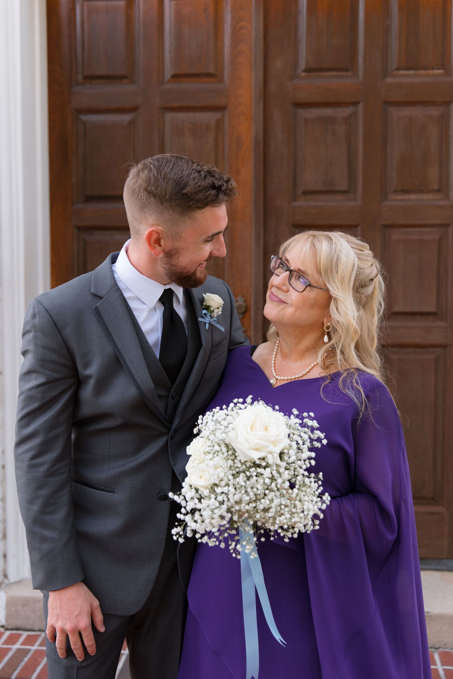 Sweet candid moment shared between two people with white floral bouquet outside church doors.
