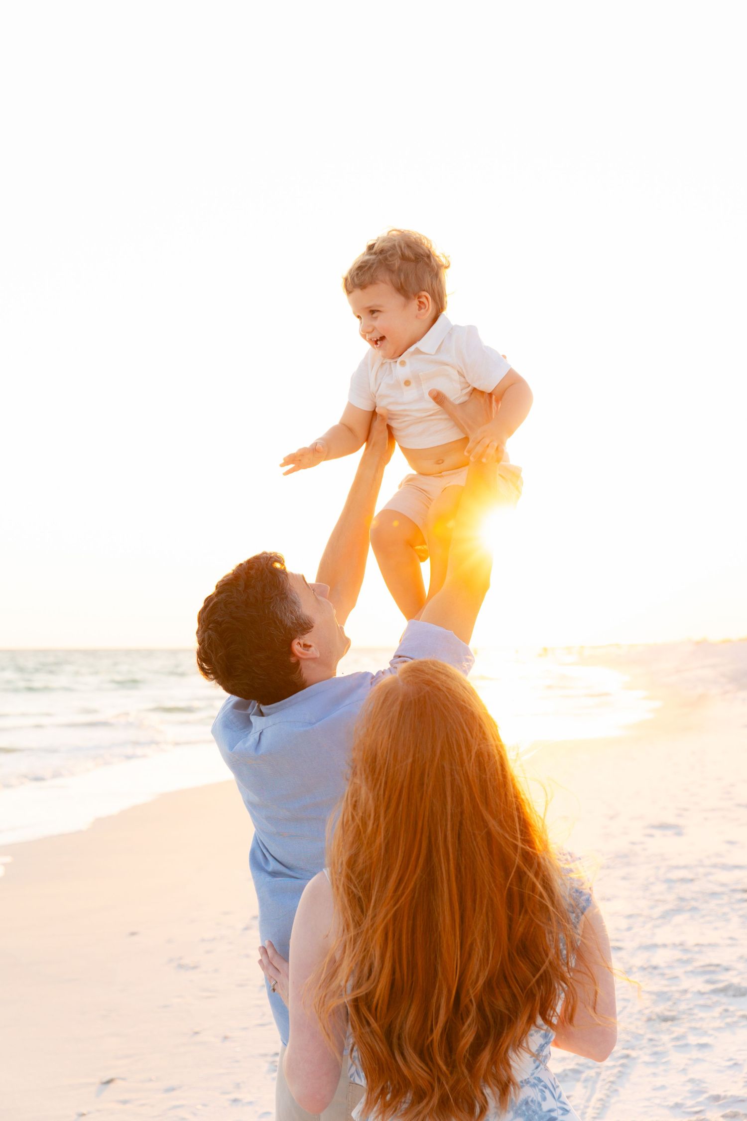 Joyful beach family moment with child being lifted at golden hour.