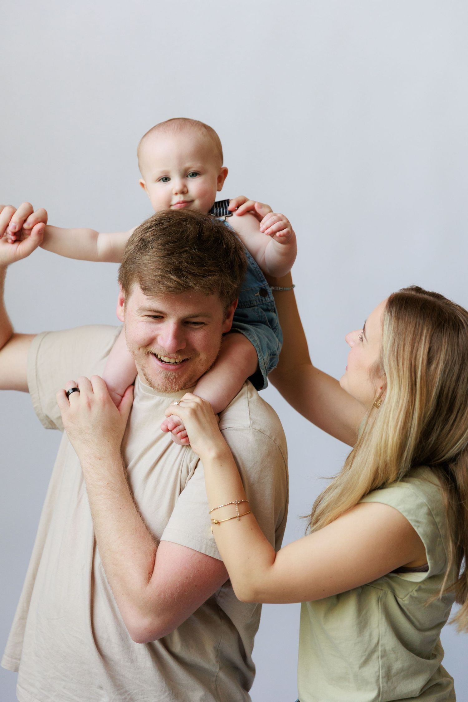A series of four sequential photos showing playful interaction between a couple and their baby in a light-filled room.