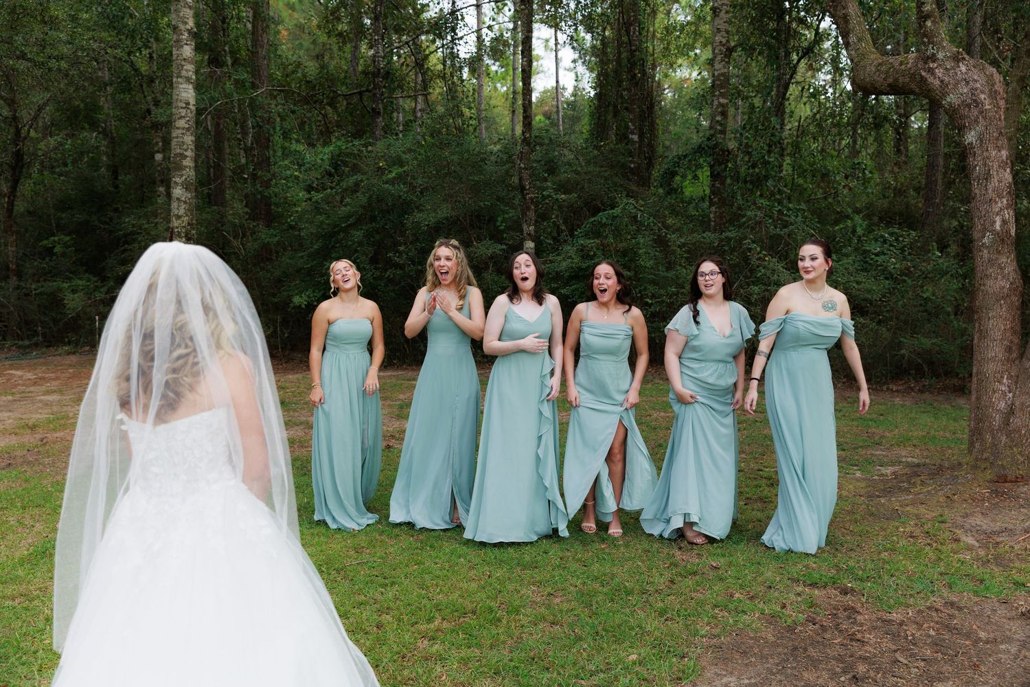 Wedding party wearing light blue bridesmaid dresses poses together in a wooded outdoor setting.