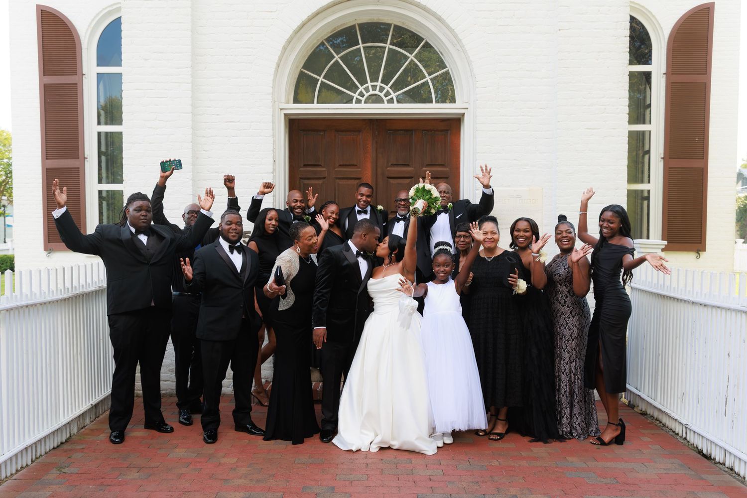 Wedding party members gather on a white porch for a formal group photo at an elegant venue.