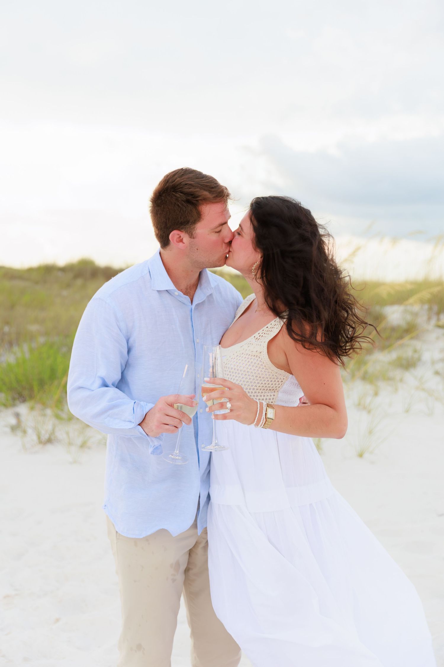 A tender beach moment between a couple in light blue and white as they share a romantic kiss.