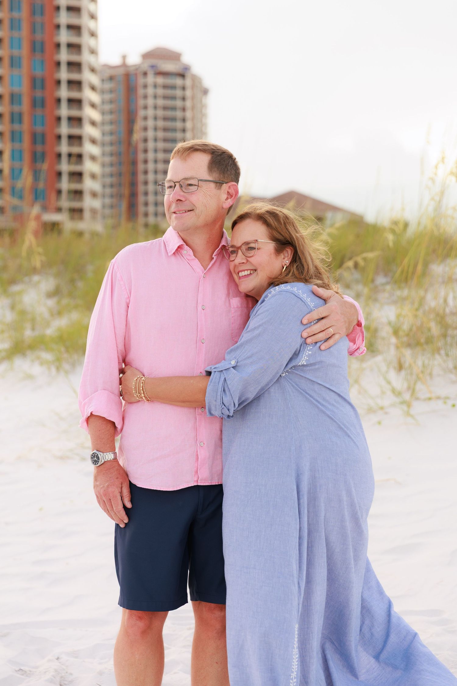 Couple sharing joyful moments on a white sandy beach with high-rise buildings in the background.