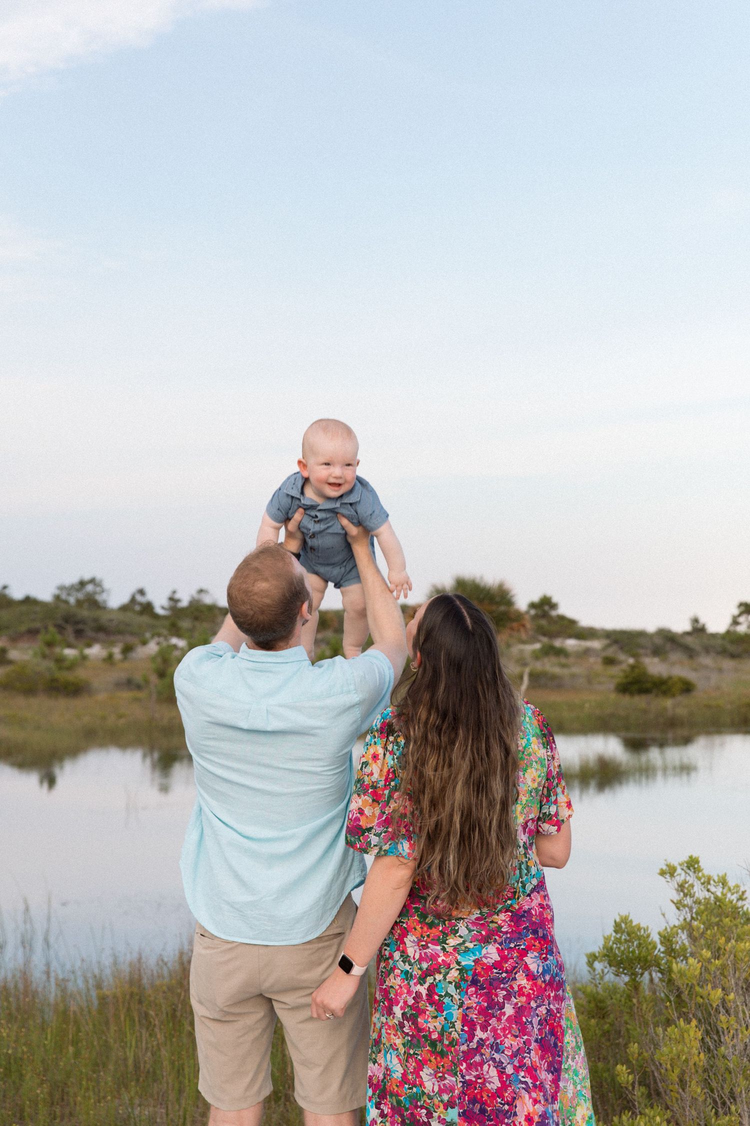Family having fun together by a tranquil waterfront with natural vegetation and clear skies.
