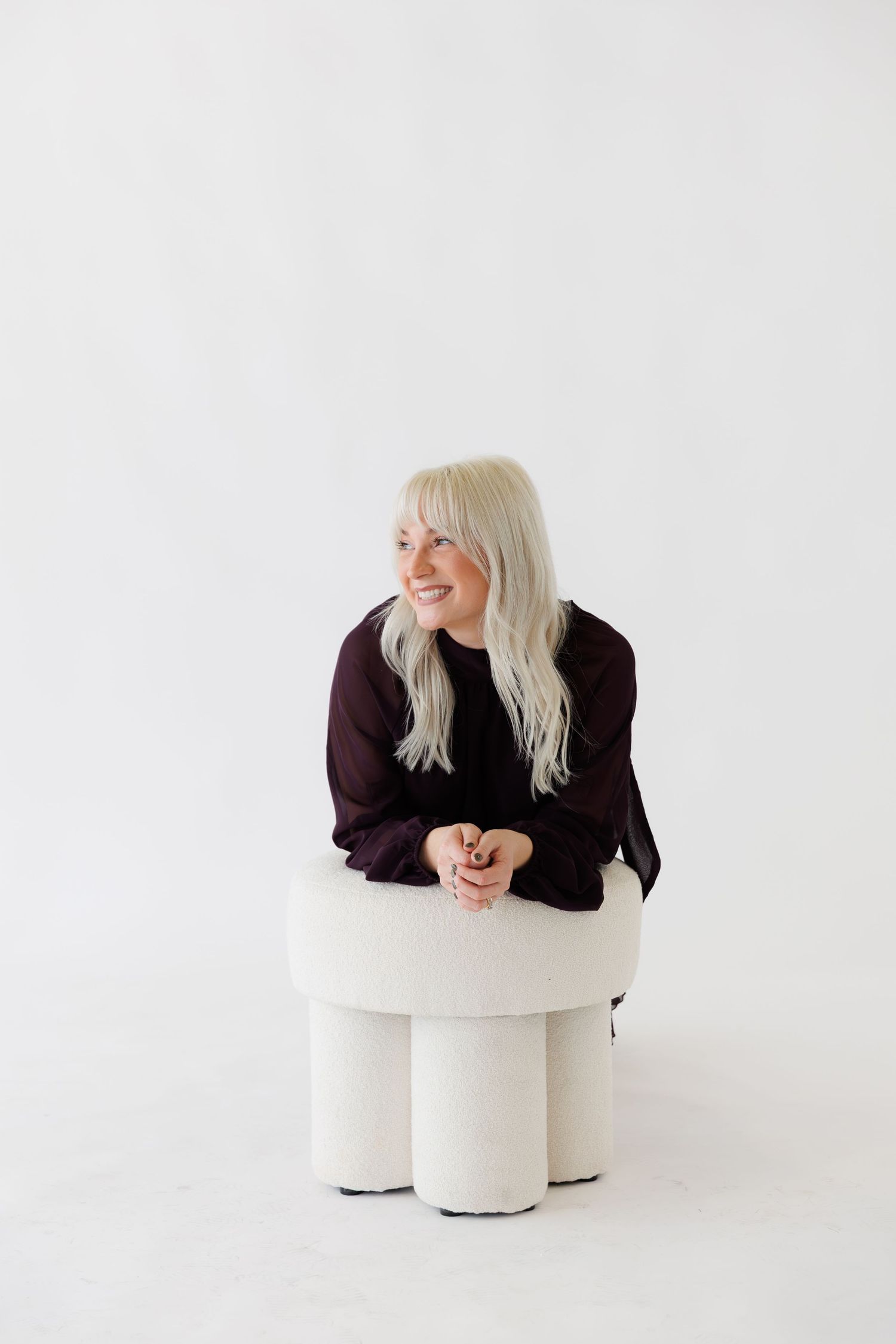 Person in purple sweater sitting on white geometric furniture piece against white background.