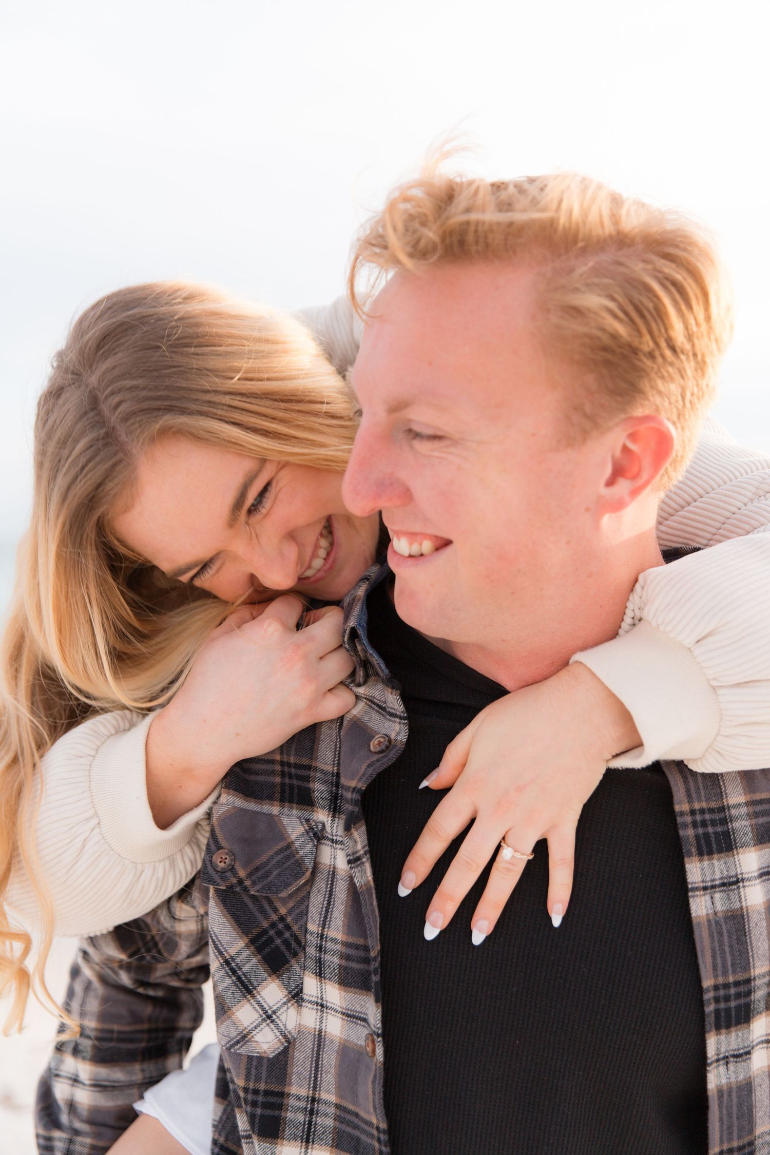 A couple shares an intimate moment while embracing, with the woman leaning into her partner wearing a plaid shirt.