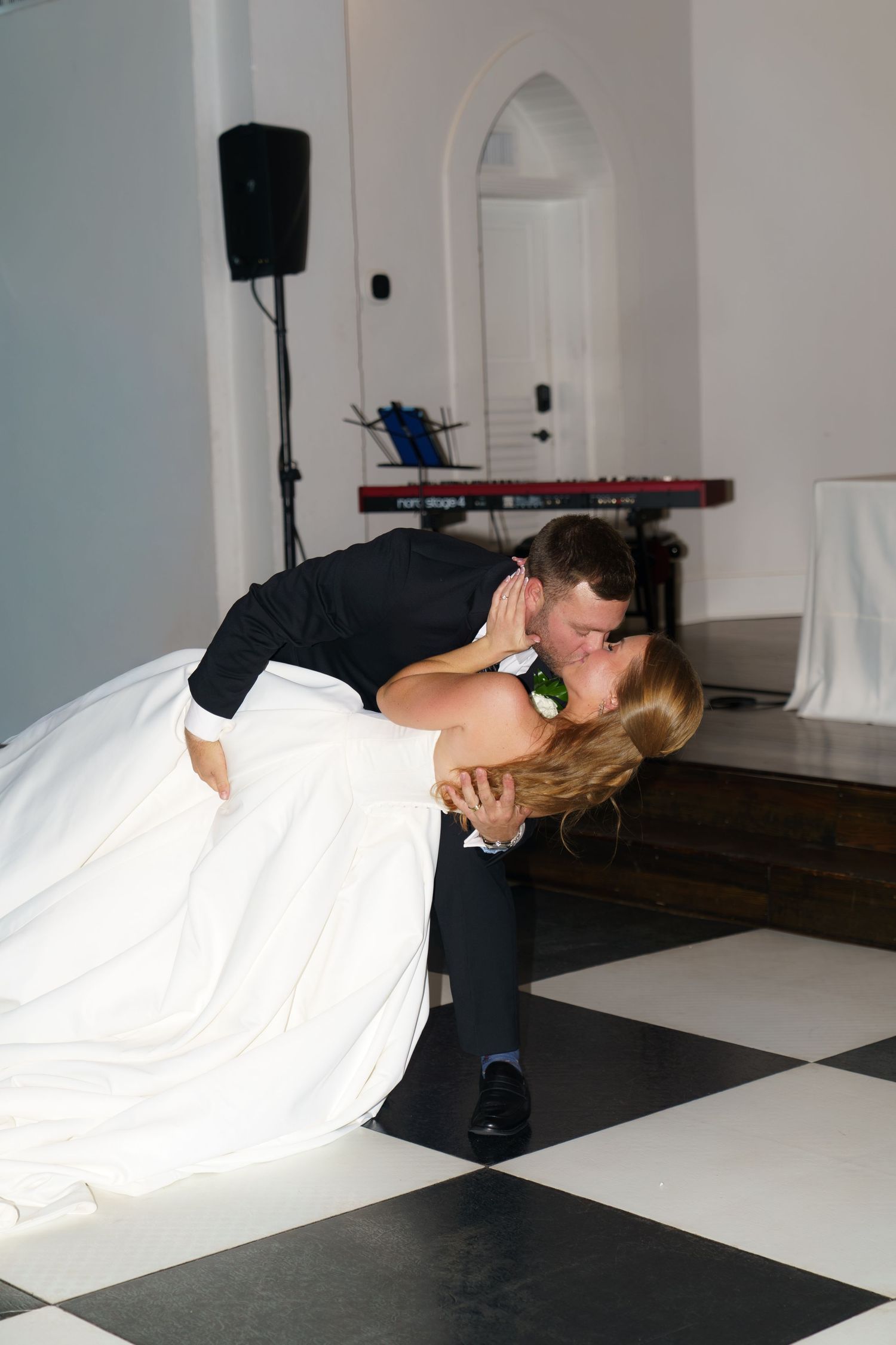 Bride and groom sharing a romantic dip kiss on a black and white checkered dance floor during their wedding reception.